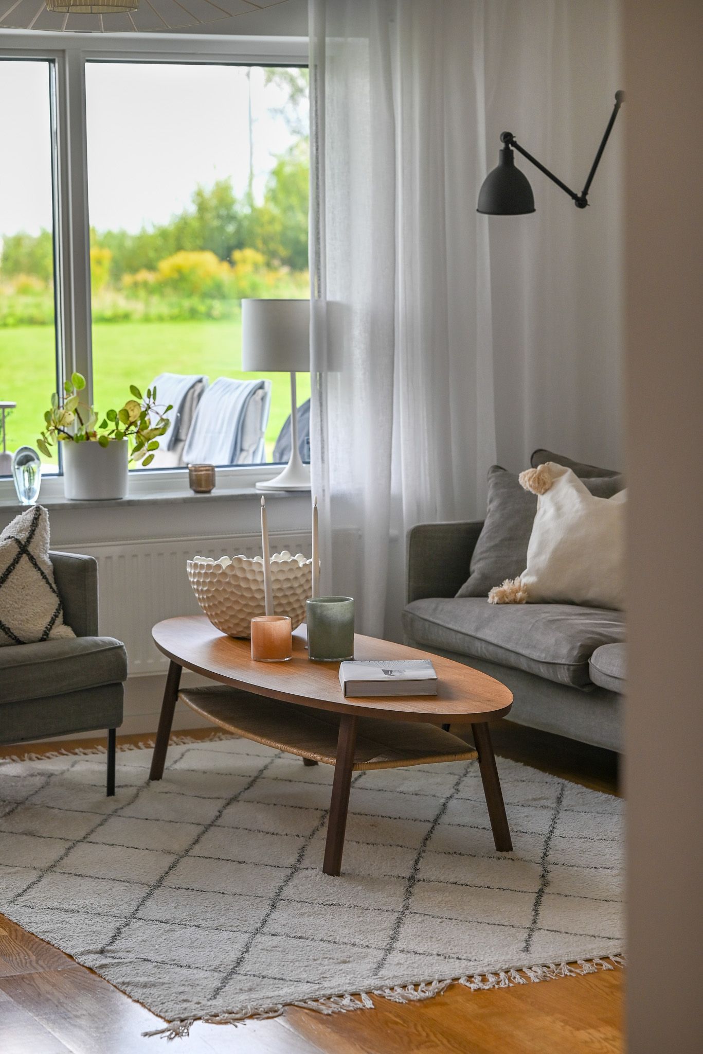 Modernt vardagsrum med mjuk matta och mysig soffhörna framför fönster med grönskande utsikt.