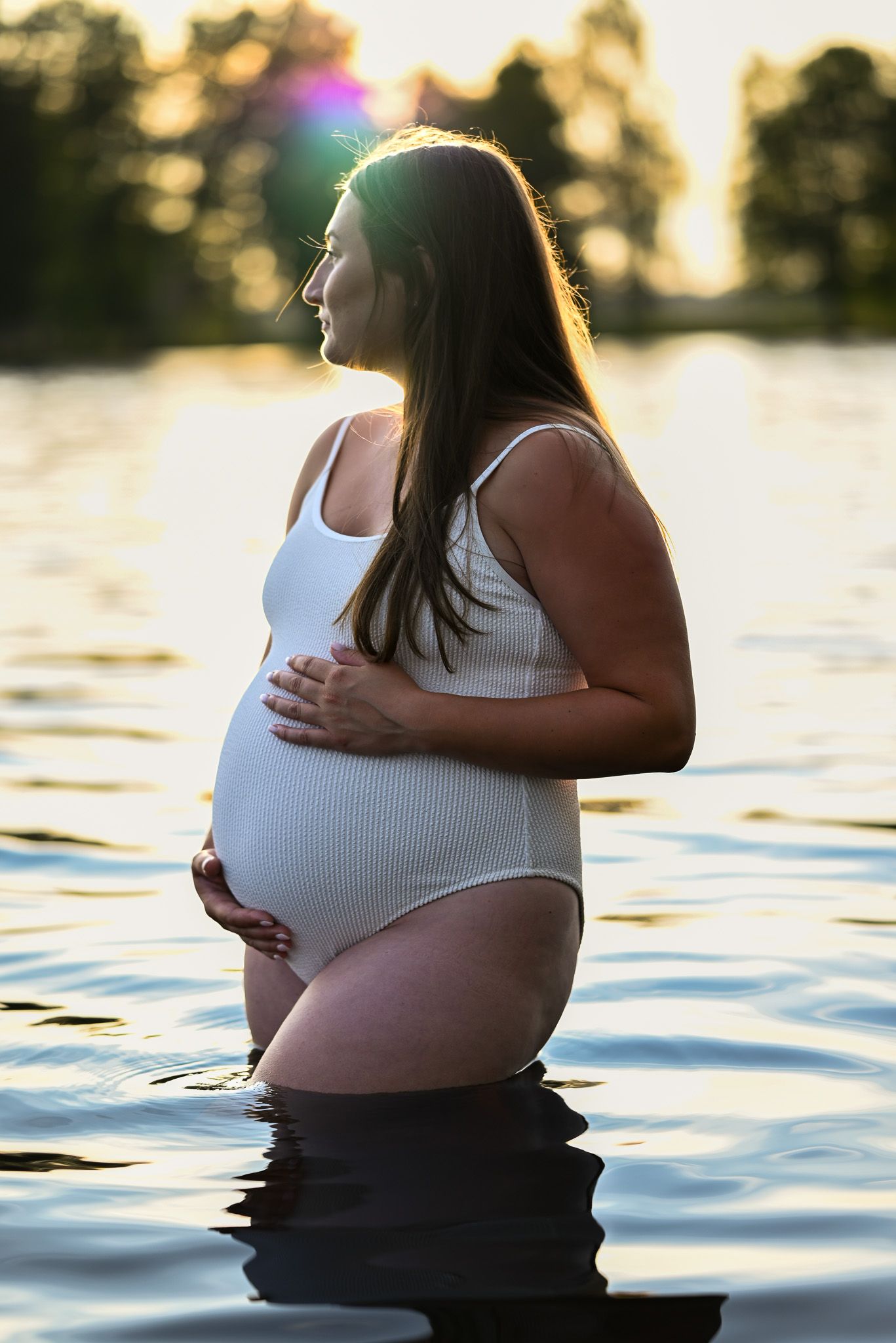 Siluett av gravid kvinna i solnedgången som fotograferas i lugnt vatten i en sjö.