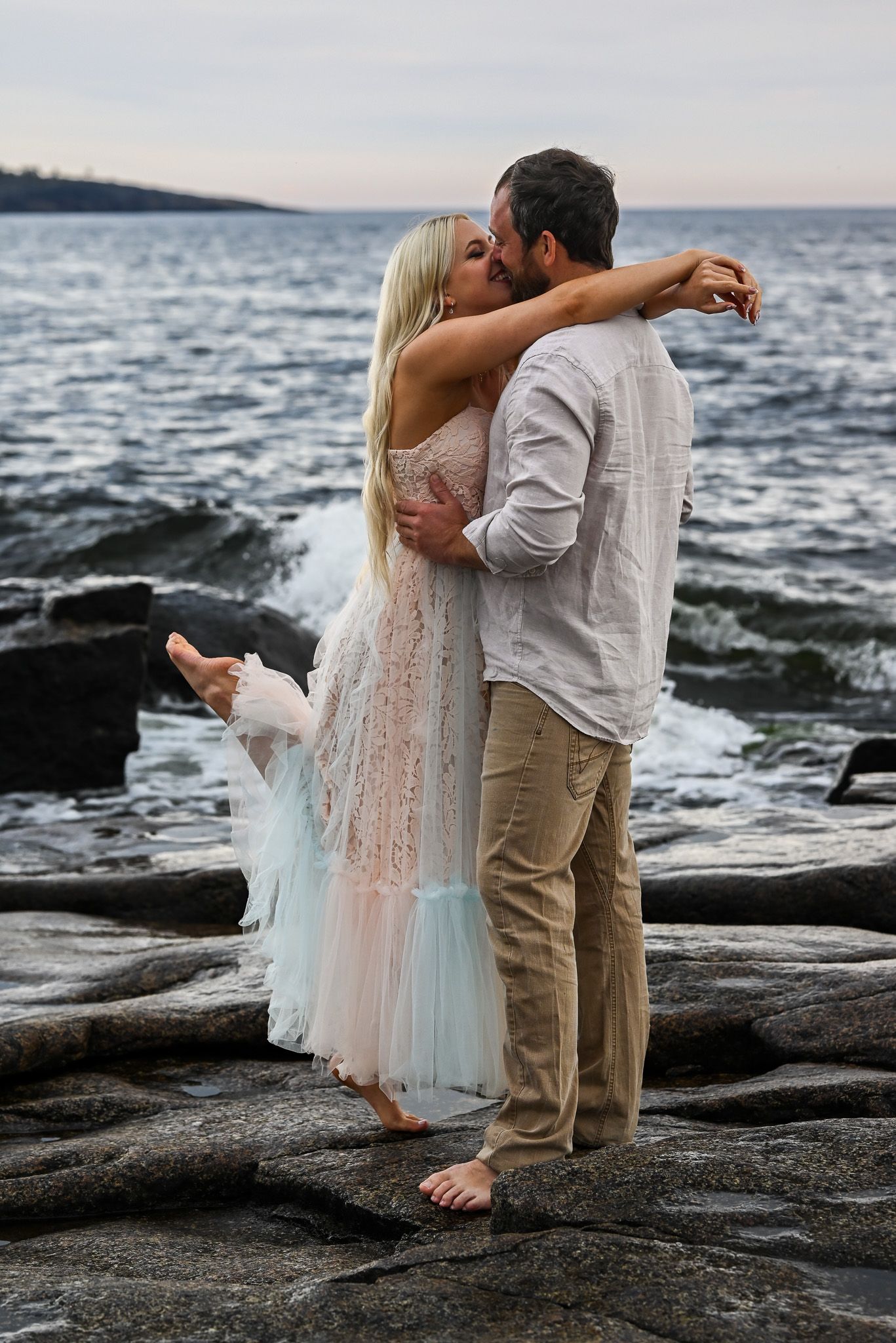 Intimt ögonblick under parfotografering vid havet med vågor som syns i bakgrunden.