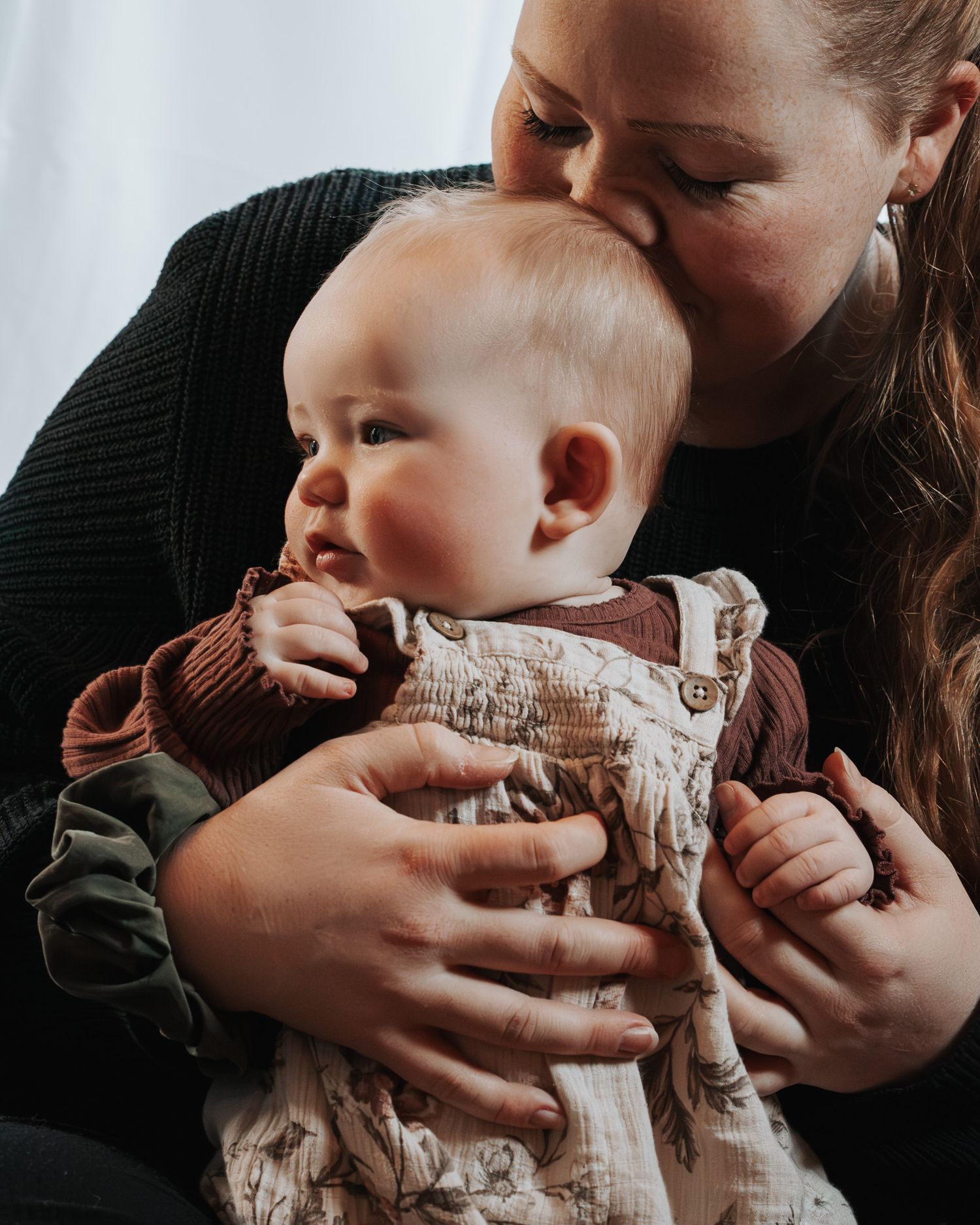 A series of intimate close-up shots showing gentle hands cradling a baby wearing a knit sweater.