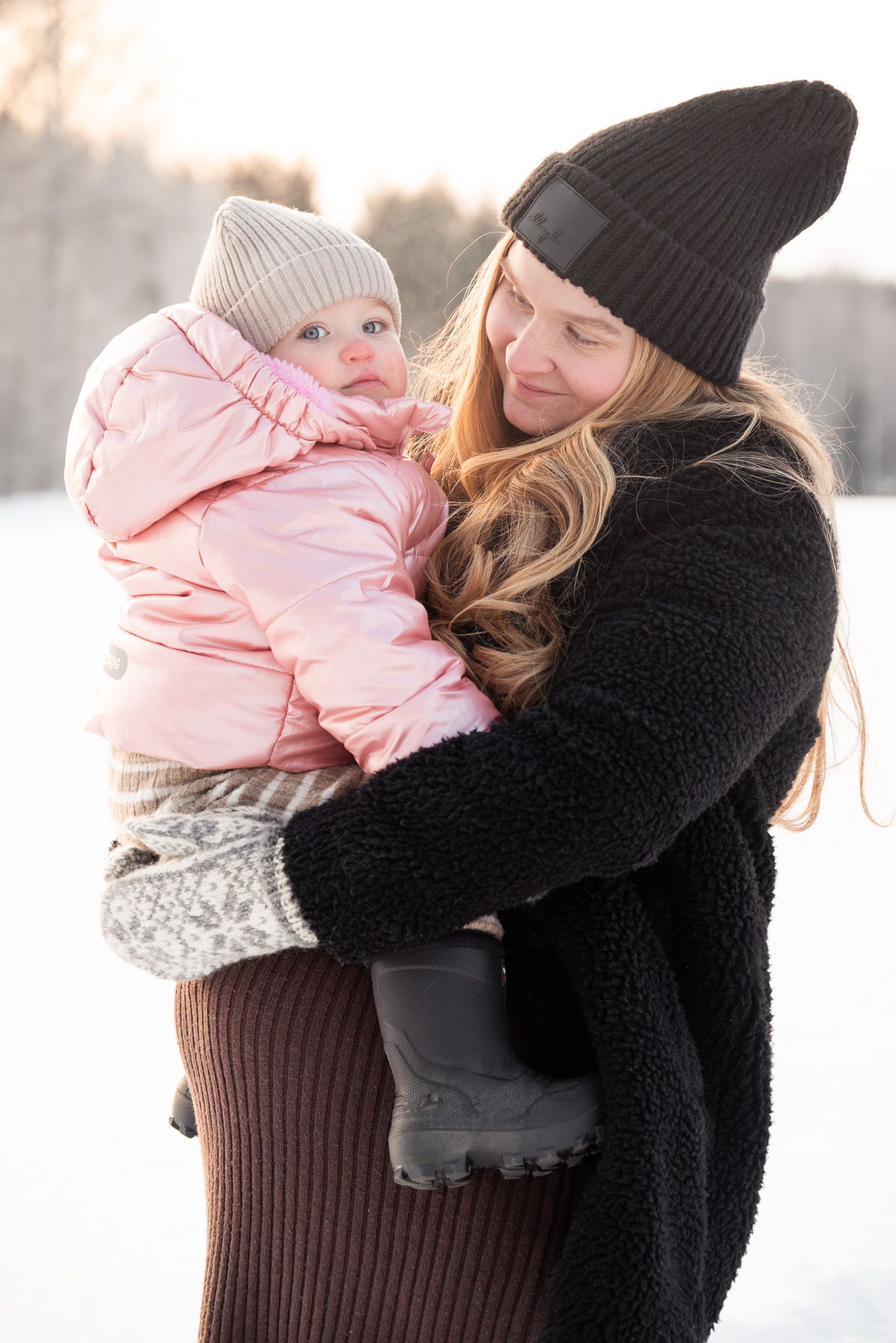 Mor och dotter i snön under gravidfotografering där även lilla dottern är med.