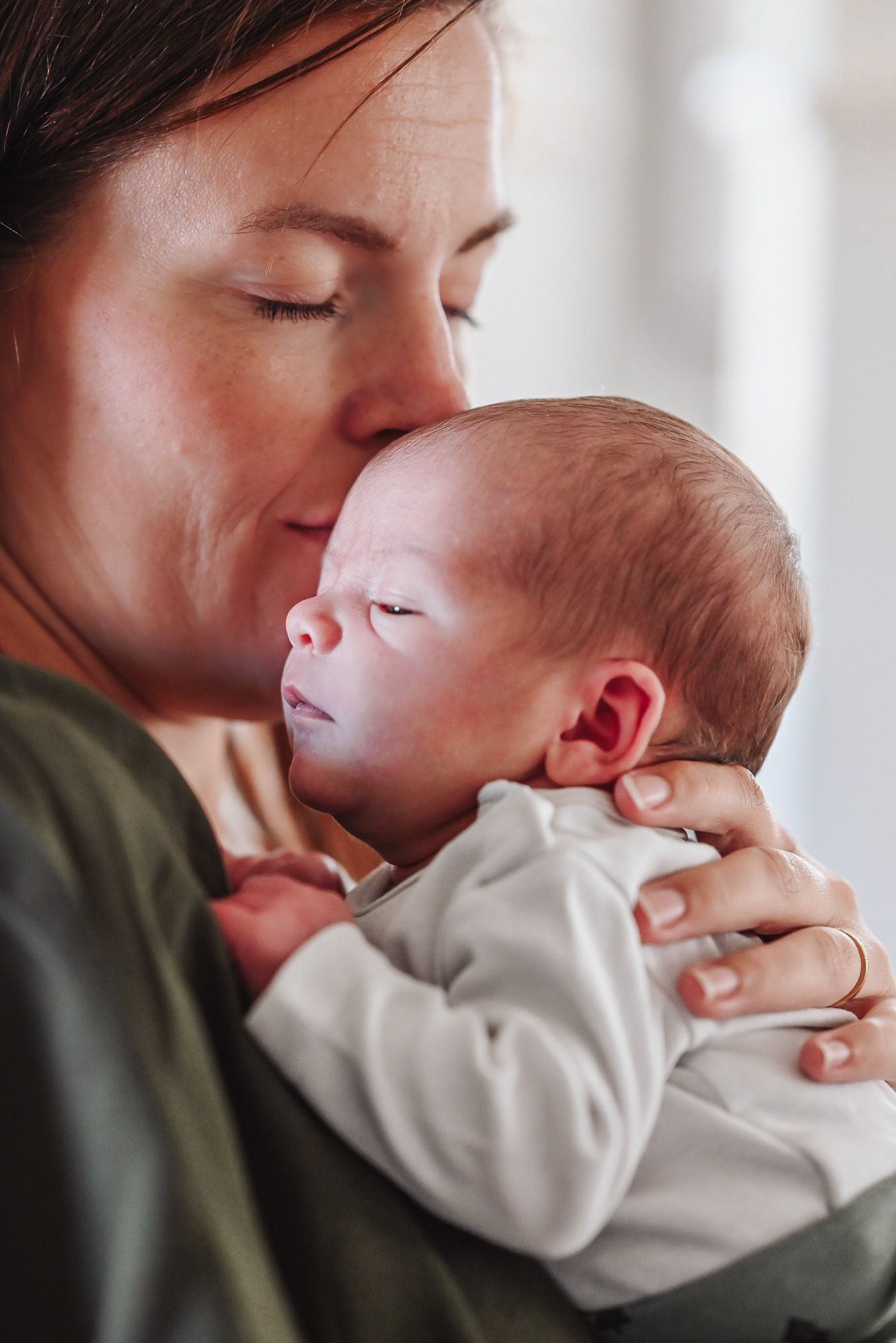 A tender moment showing parent gently kissing and holding a sleeping baby in white clothing.