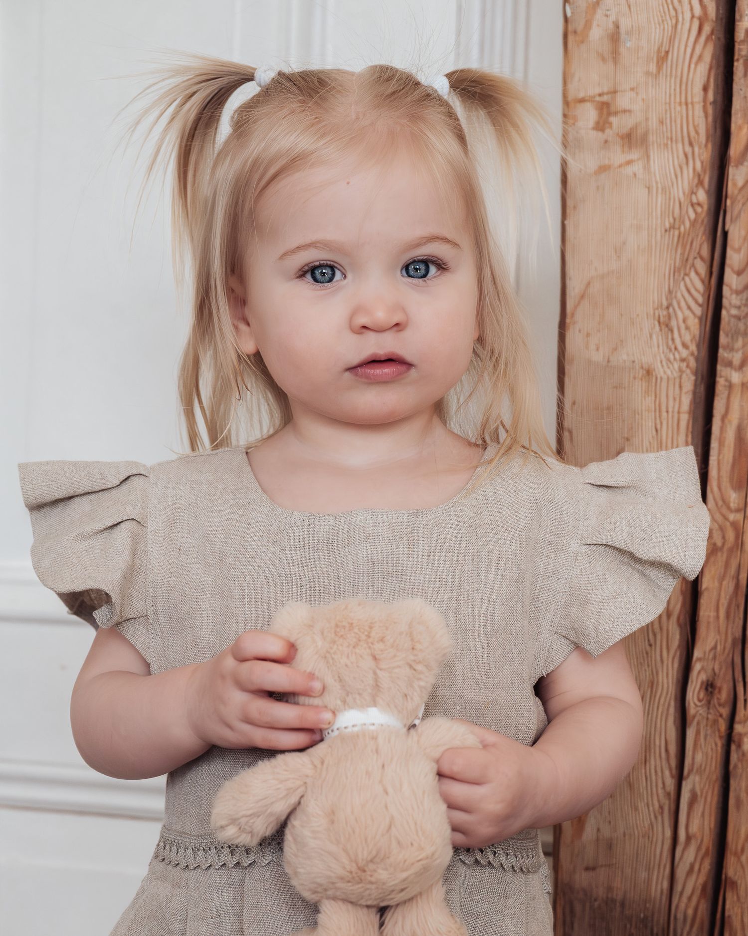 Liten tjej med tofsar håller i sin nalle och ser in i kameran under nyföddfotografering.