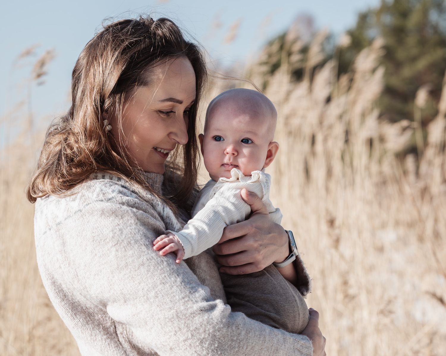 A parent and baby share tender moments in a field of tall golden grass during a warm autumn day.