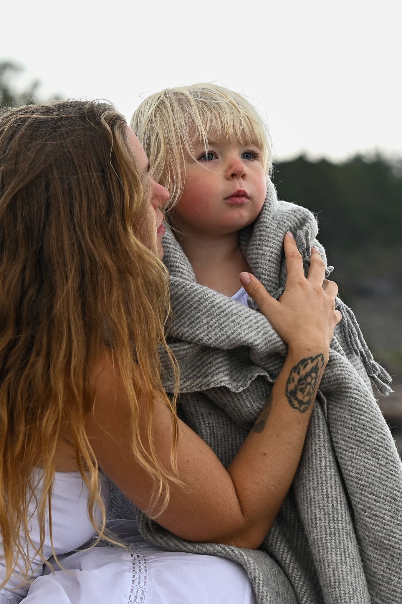 Kärleksfullt porträtt mellan mor och dotter i varma toner intill havet i solnedgången.