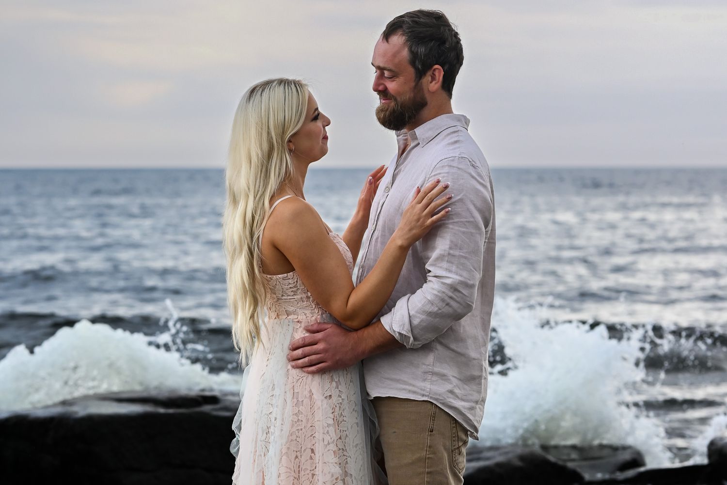 Kärleksfullt par delar romantisk stund vid havet med vågor i bakgrunden i solnedgången.