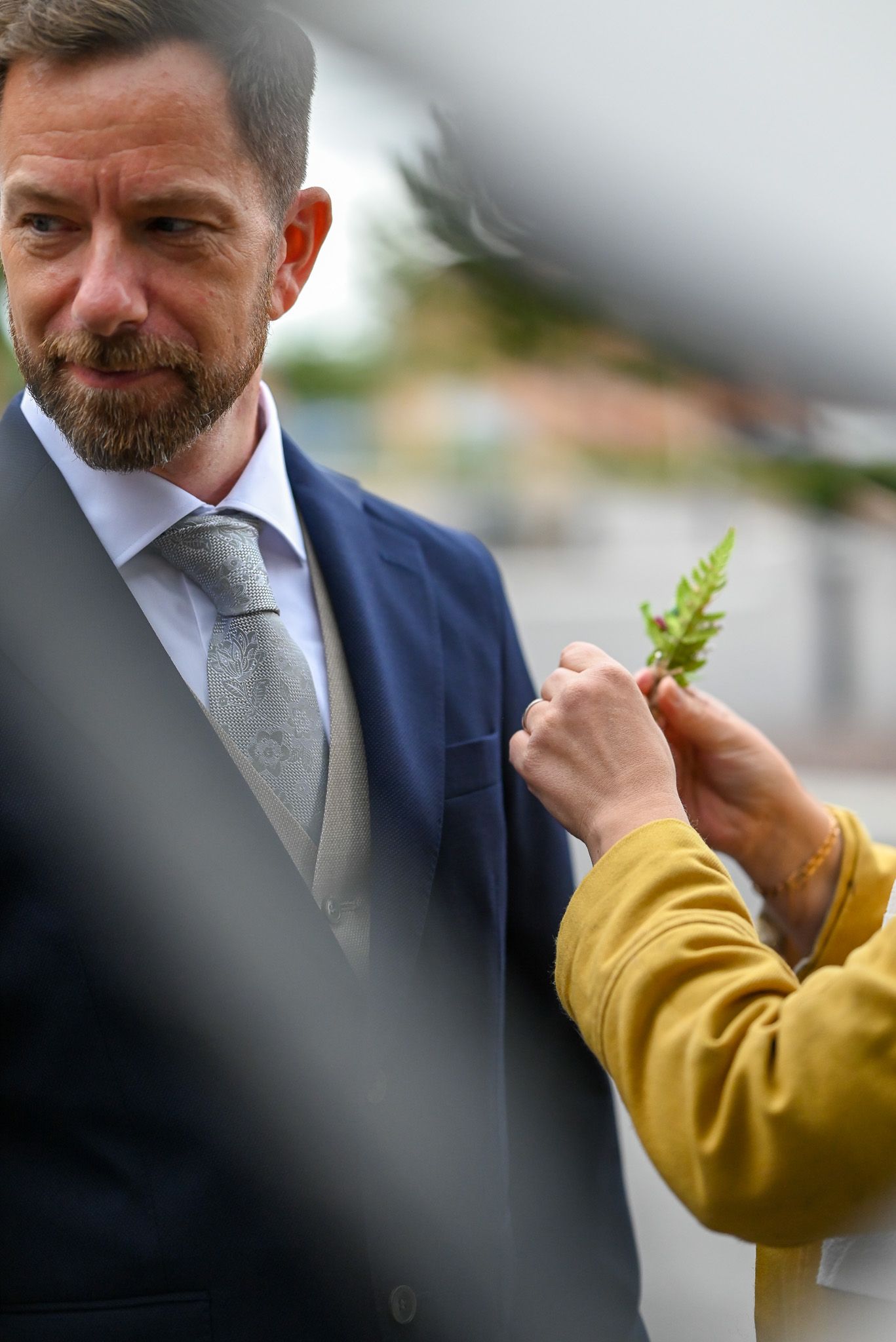 Detailjfoto av brudgum som får blommor på kragen.