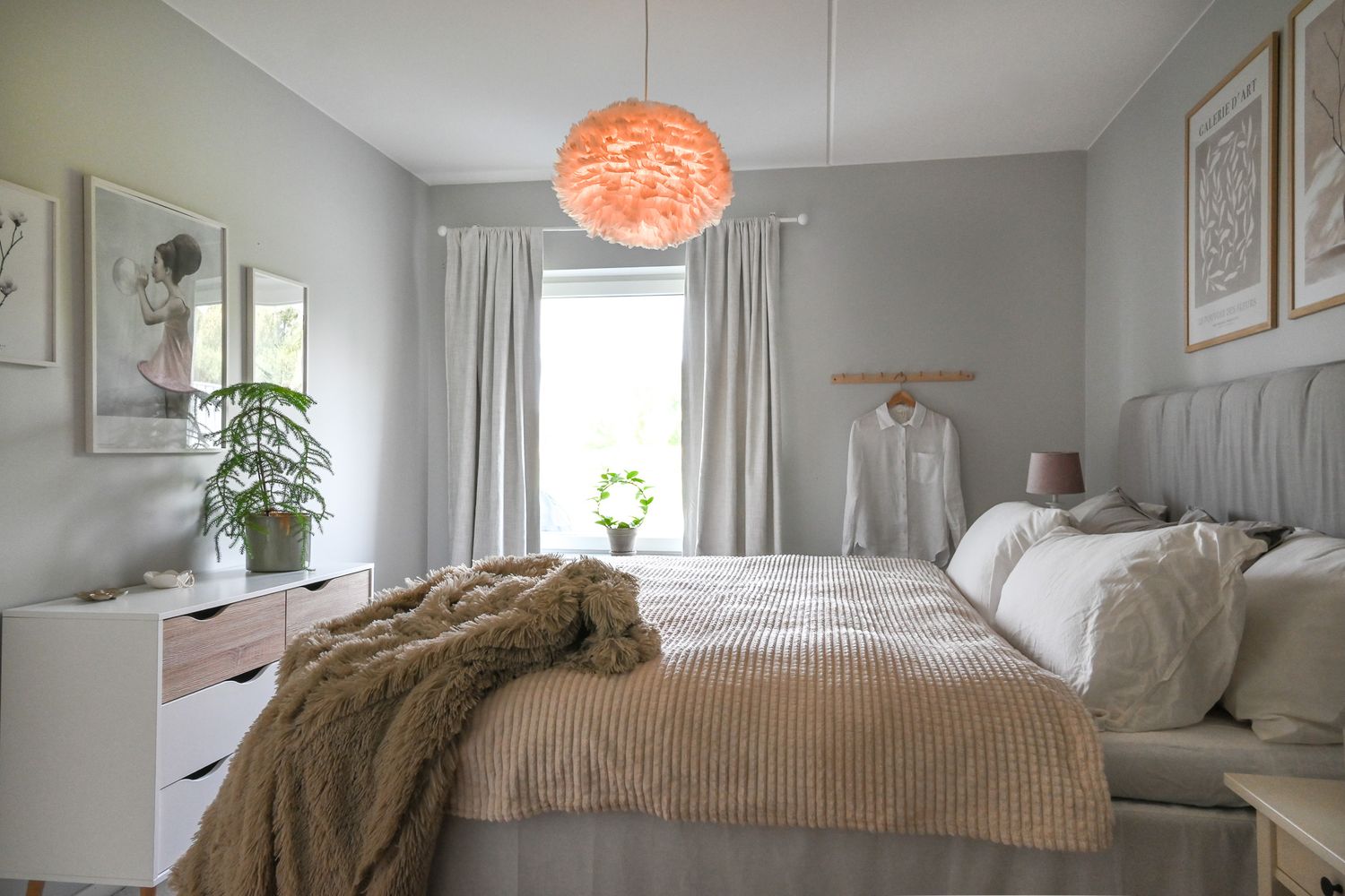 Mysigt sovrum med fluffigt täcke och inbjudande kuddar för god natt sömn, grå väggar och fjäderlampa med gröna växter höjer mysfaktorn.