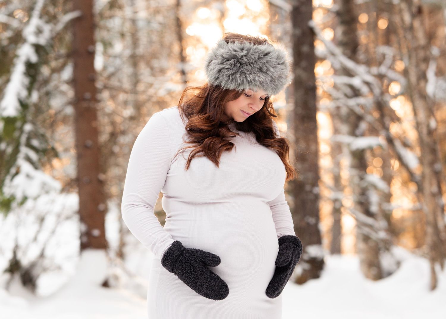 Gravid kvinna håller om magen under vinterfotografering i varmt motljus.