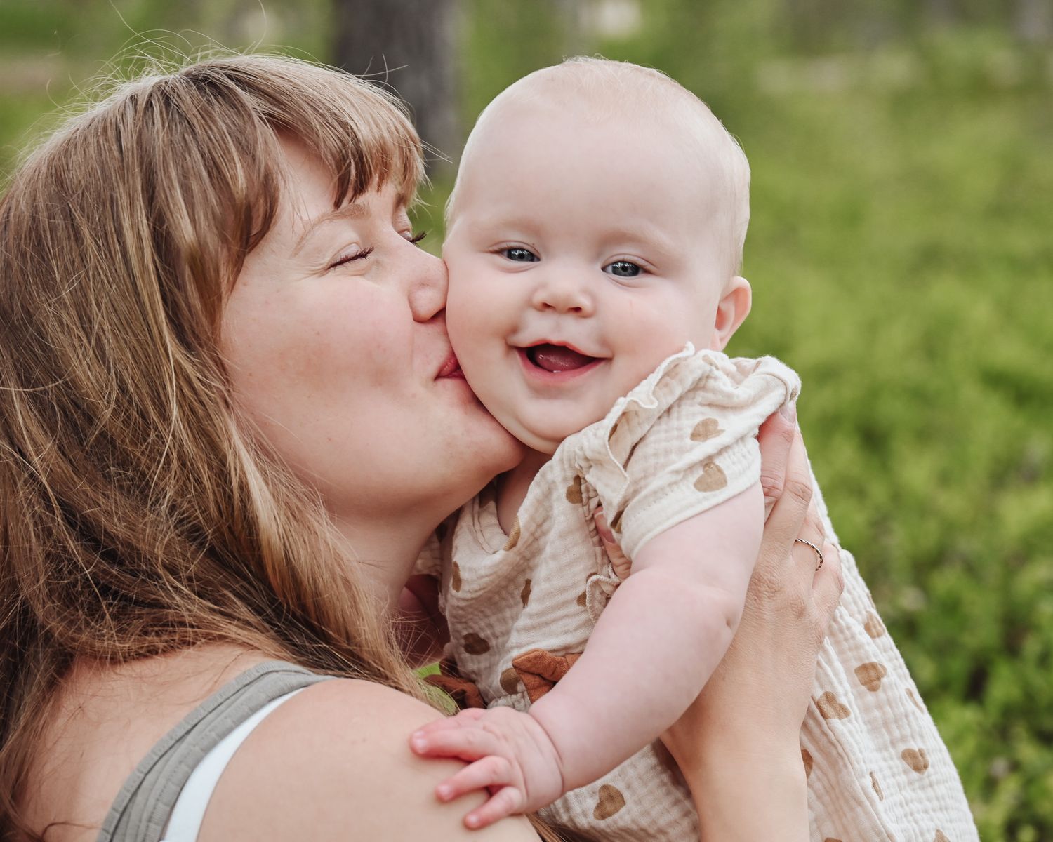 A tender moment between parent and baby in a grassy outdoor setting on a sunny day.