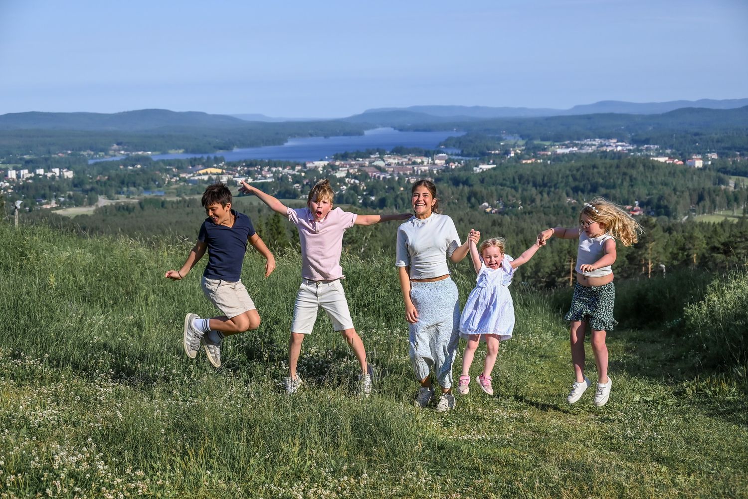 Syskon leker med storslagen bakgrund i bergen en solig dag i grönskande gräs.