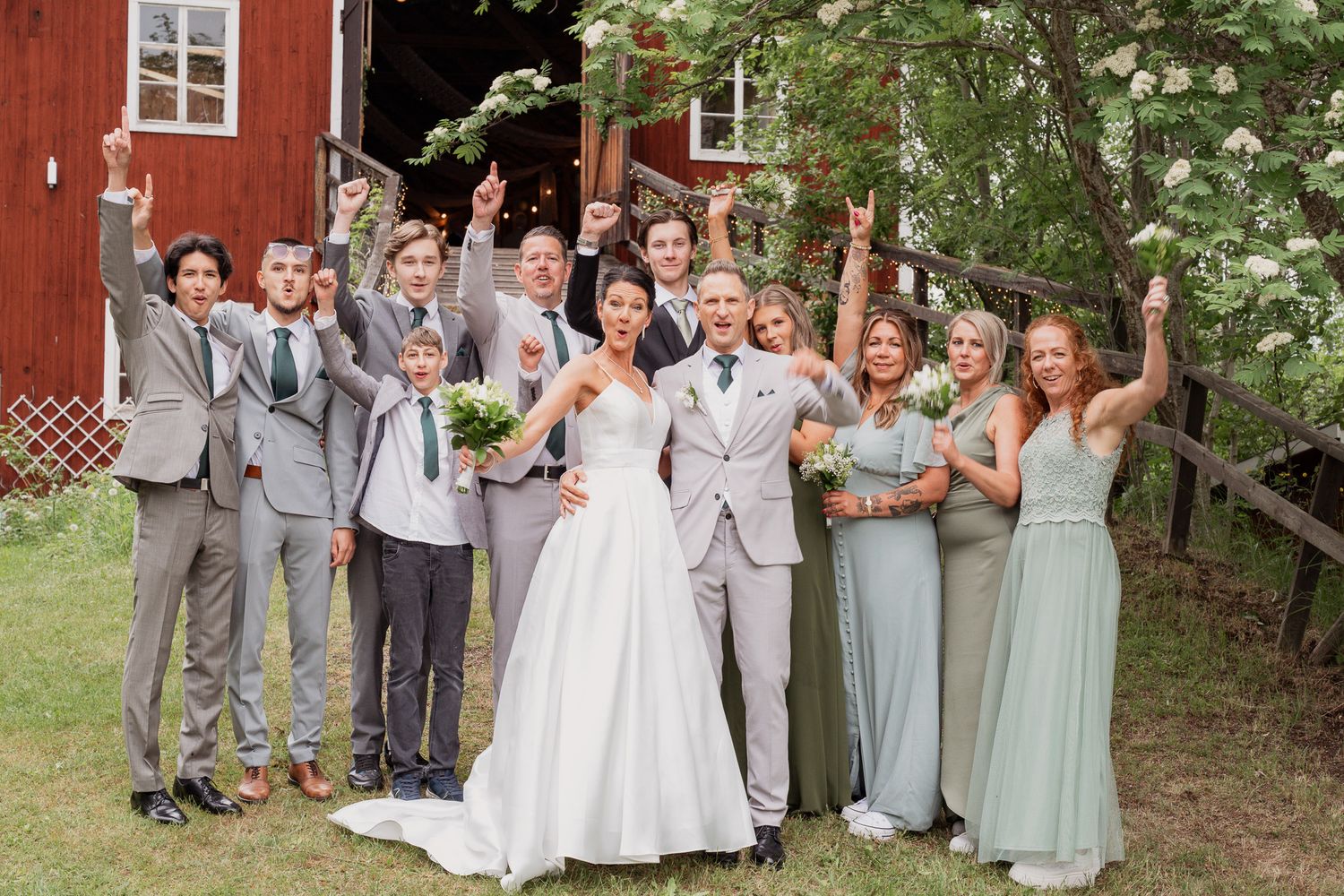 Gruppfoto på bröllop med firande brudsällskap utanför festlokal.