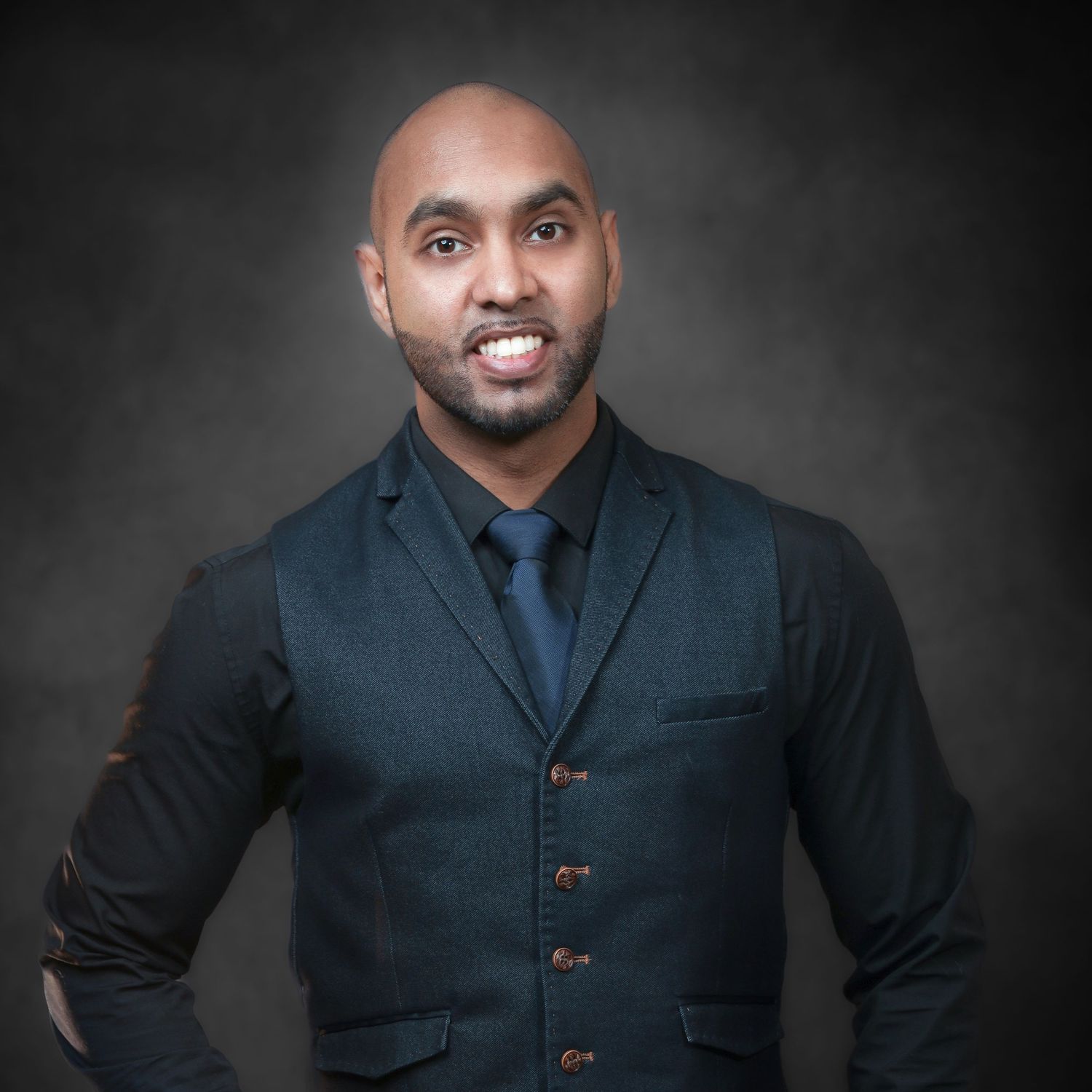 Kamal in a dark blazer and tie smiles against a gray studio background. Aerial Site Intelligence