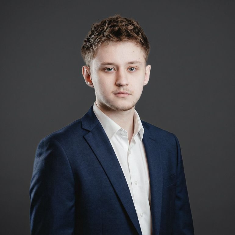 Larno in navy blazer and white shirt poses for formal headshot against gray background.