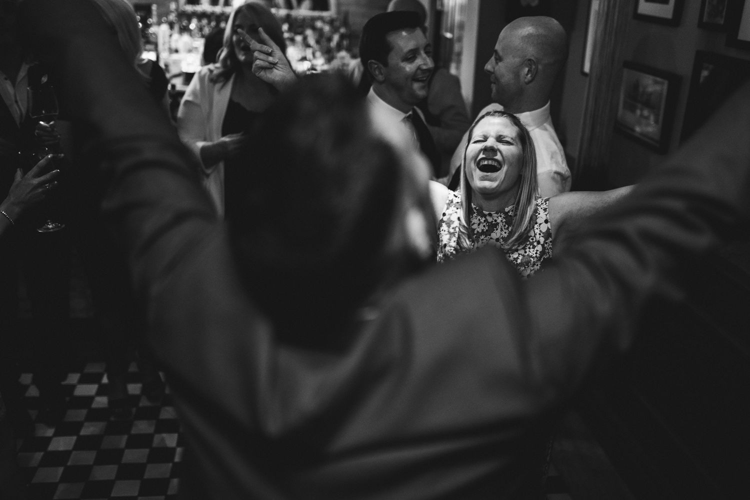 A joyful scene captured in black and white shows a person laughing amid a crowded indoor space.