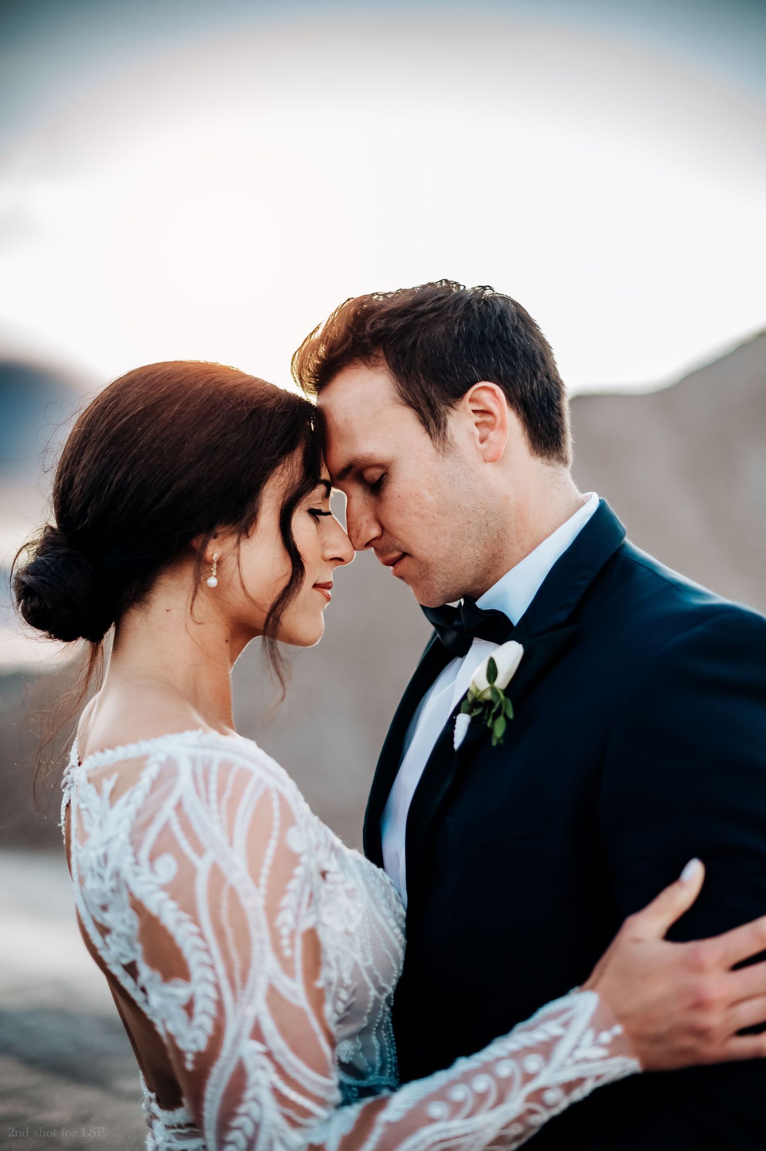 A bride and groom in elegant wedding attire share an intimate forehead-to-forehead moment outdoors at golden hour in Holland Michigan.