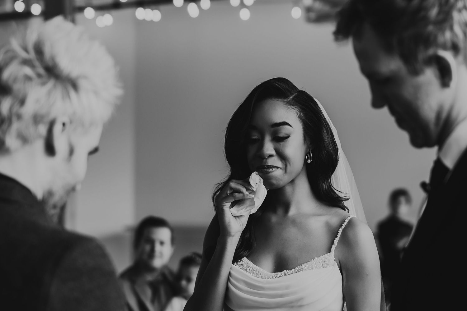 Black and white photo of an emotional bride wiping tears during her wedding ceremony.