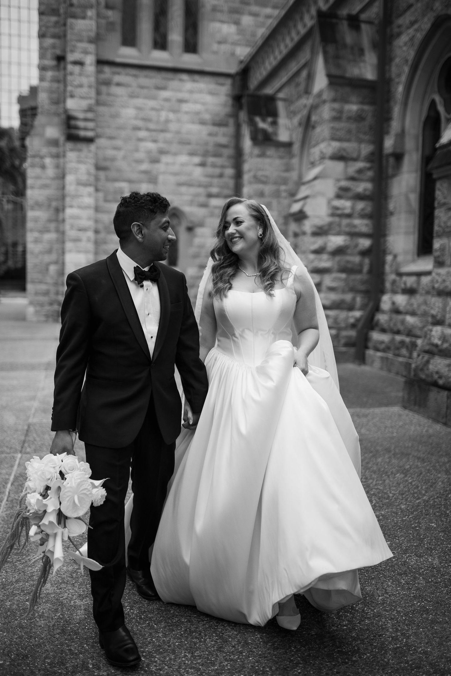 A young boy in a suit walks alongside a bride in a white wedding dress outside a stone church.