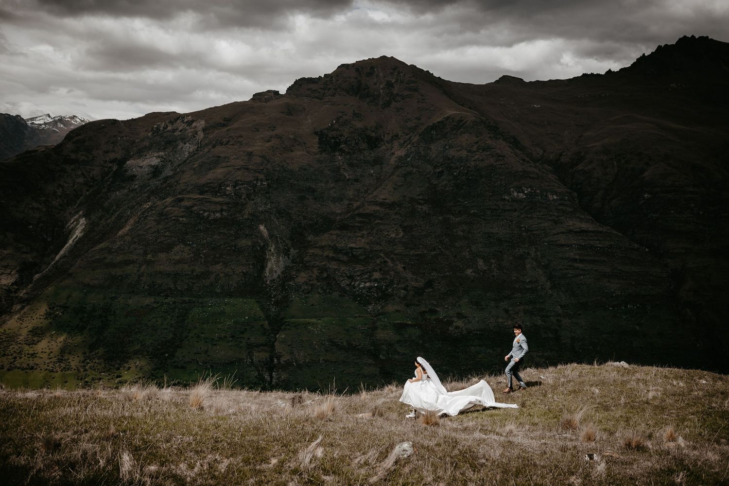 A dramatic mountain landscape with dark storm clouds gathering overhead and rugged peaks in the distance.