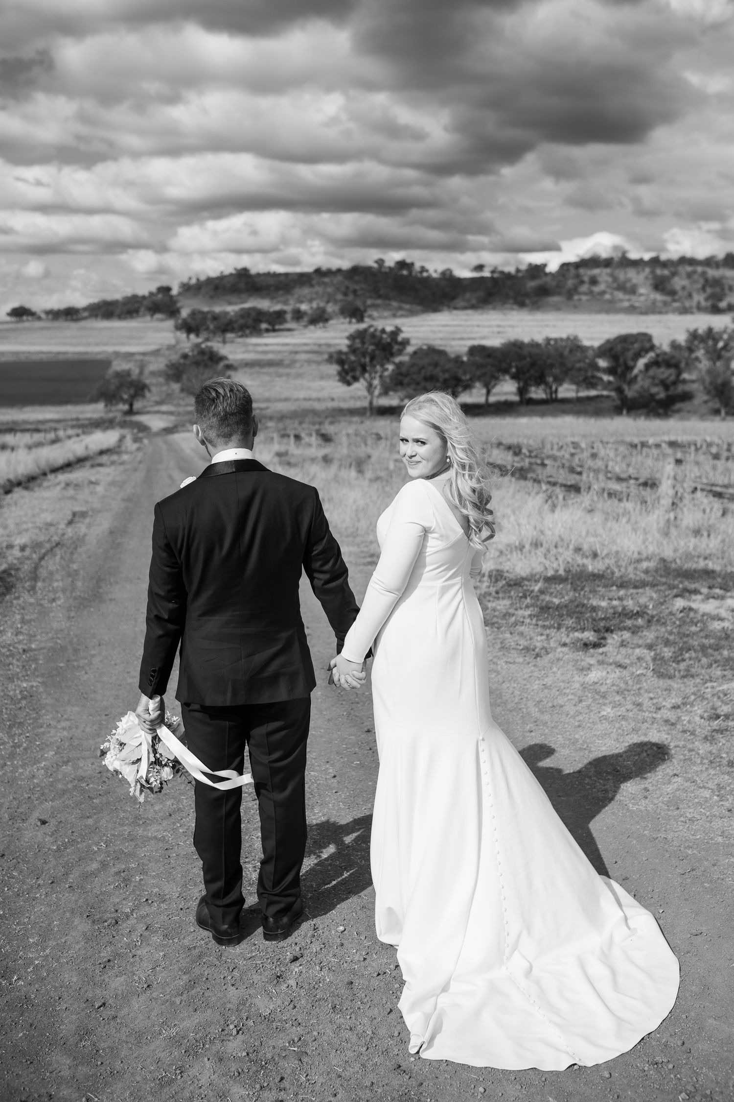 A couple walks through a dramatic landscape with rolling hills and moody clouds in black and white photography.