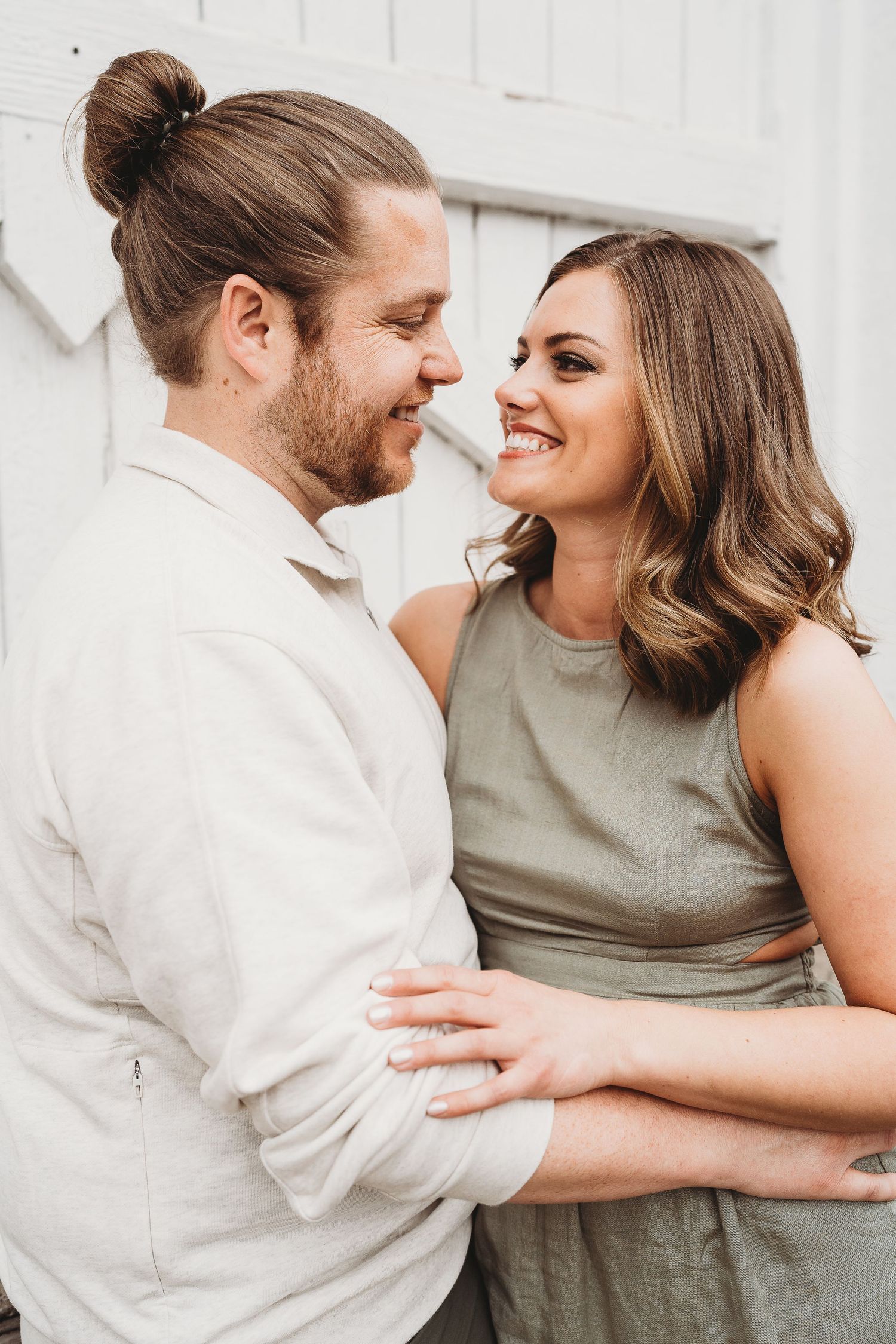 Romantic portrait of a couple smiling and embracing against a white wall.