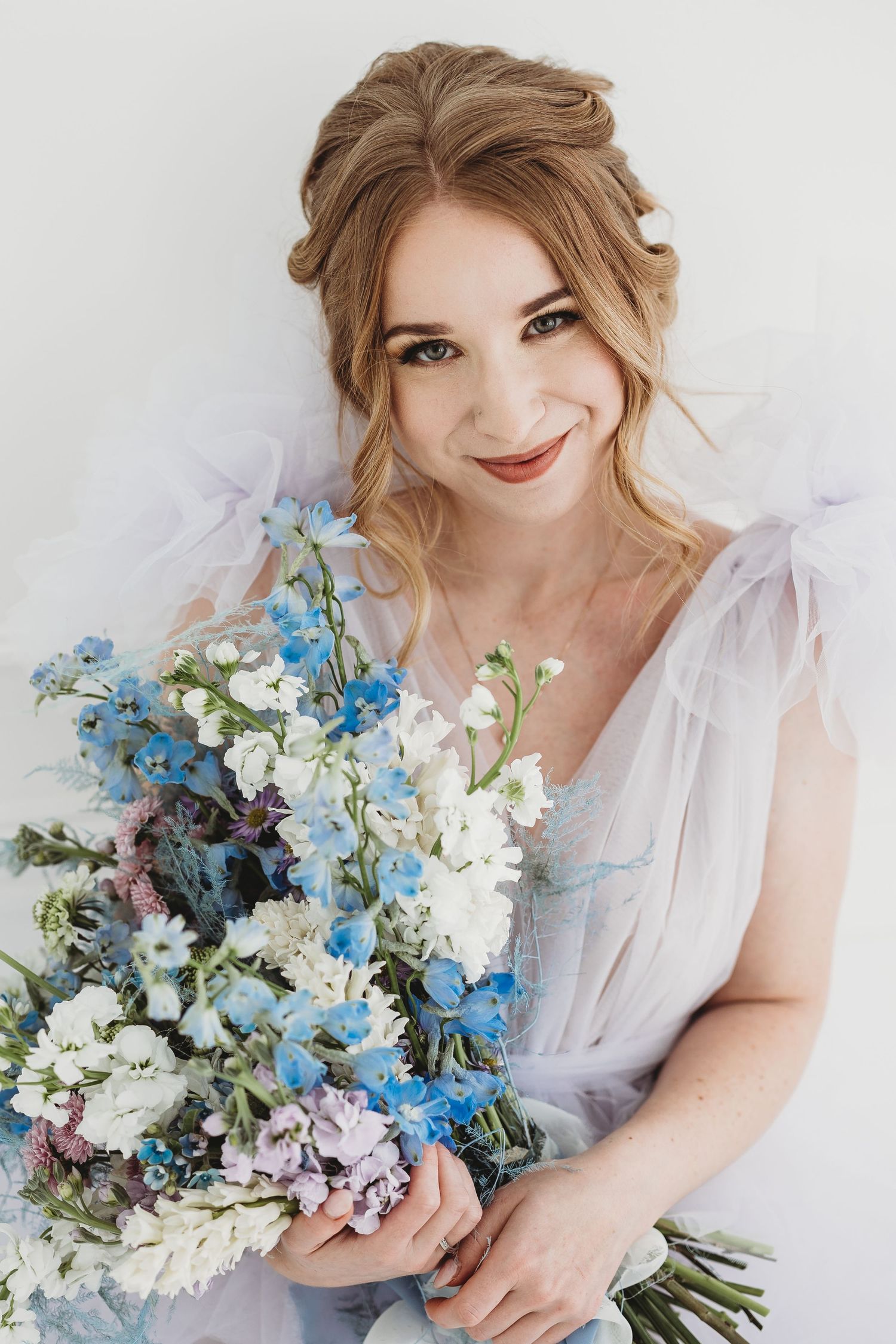 Ethereal bridal portrait featuring an elegant bouquet of blue delphinium and white flowers against a light background.