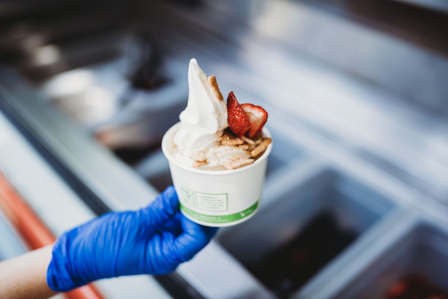 Finished ice cream dessert with strawberry and wafer toppings held by blue gloved hand.