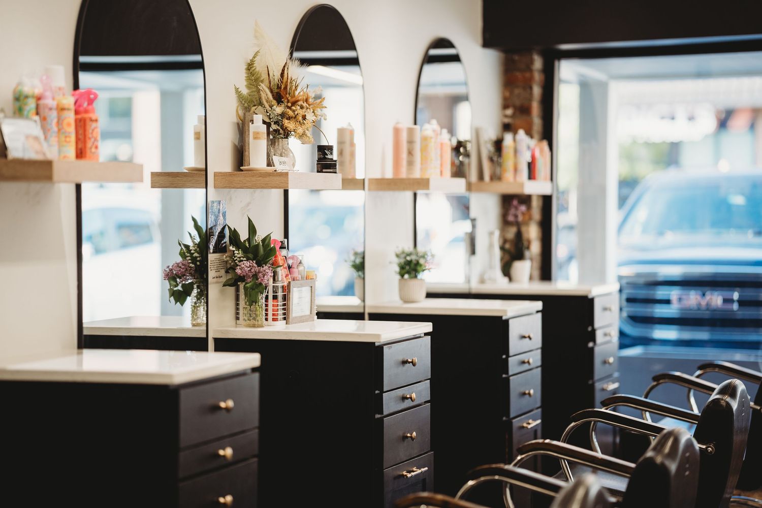 Hair salon workspace with black styling stations and arched mirrors in natural daylight.
