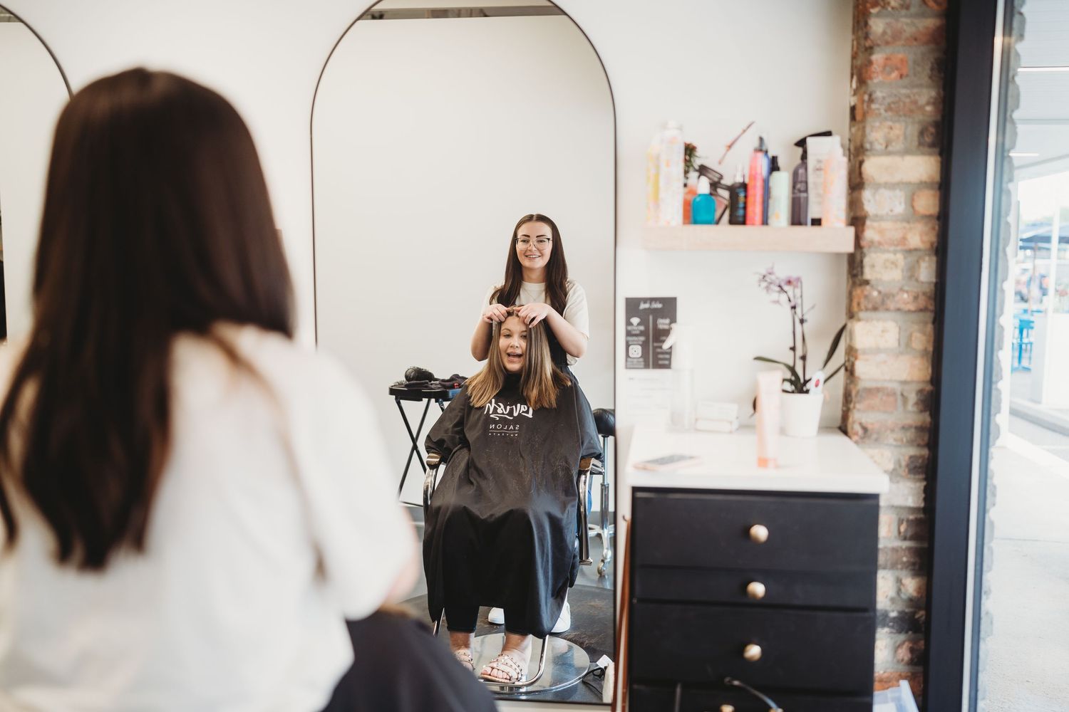 Mirror reflection of hairdressing session in modern salon with minimalist design.