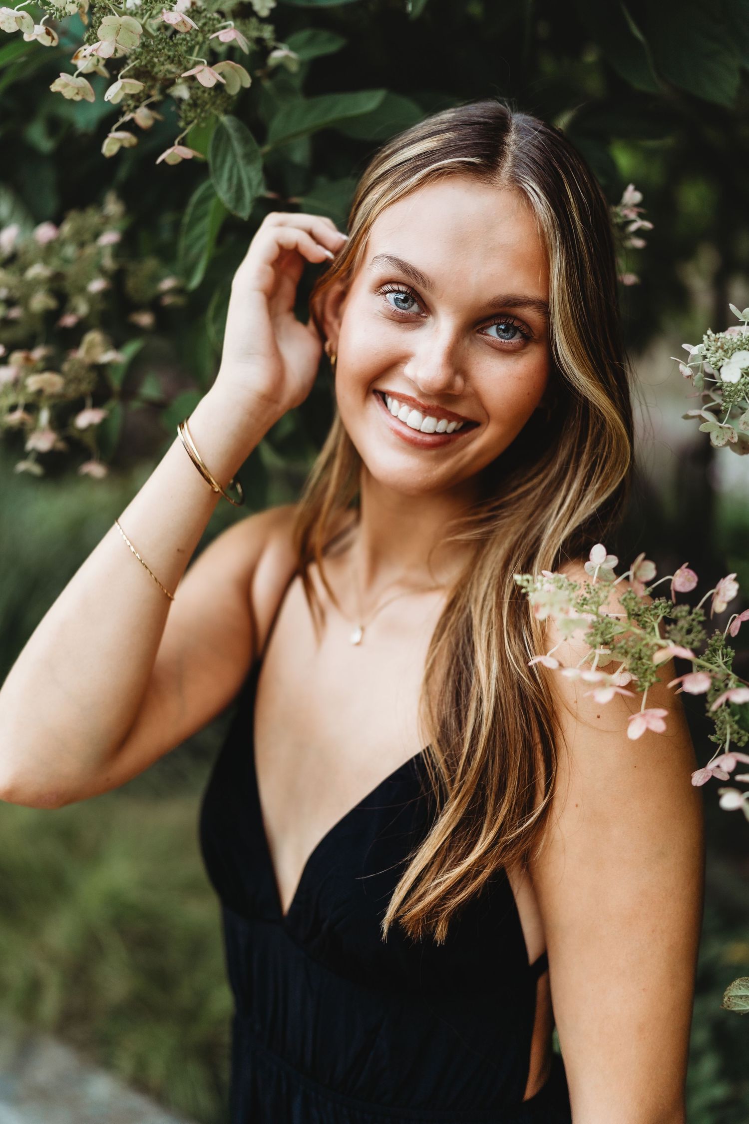 A woman in a black top poses with blooming white flowers in a spring outdoor portrait session.