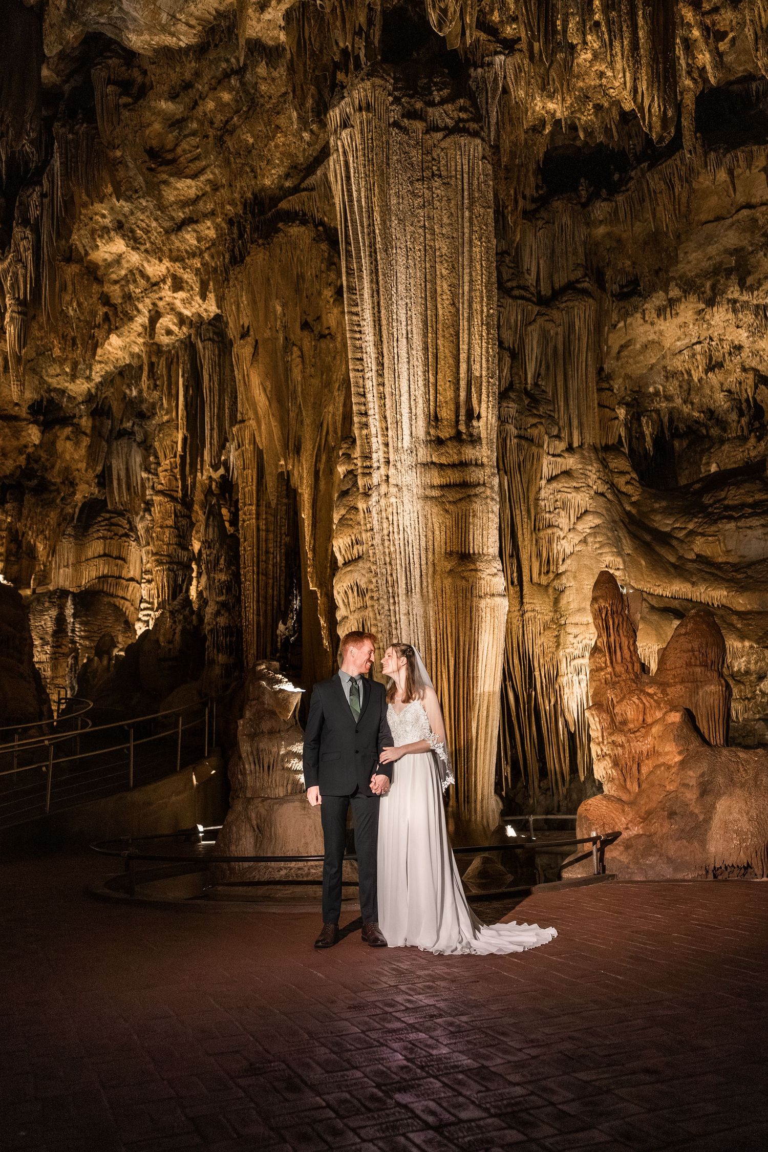 A couple shares an intimate moment during their wedding ceremony in a dramatic underground cave with illuminated stalactites.