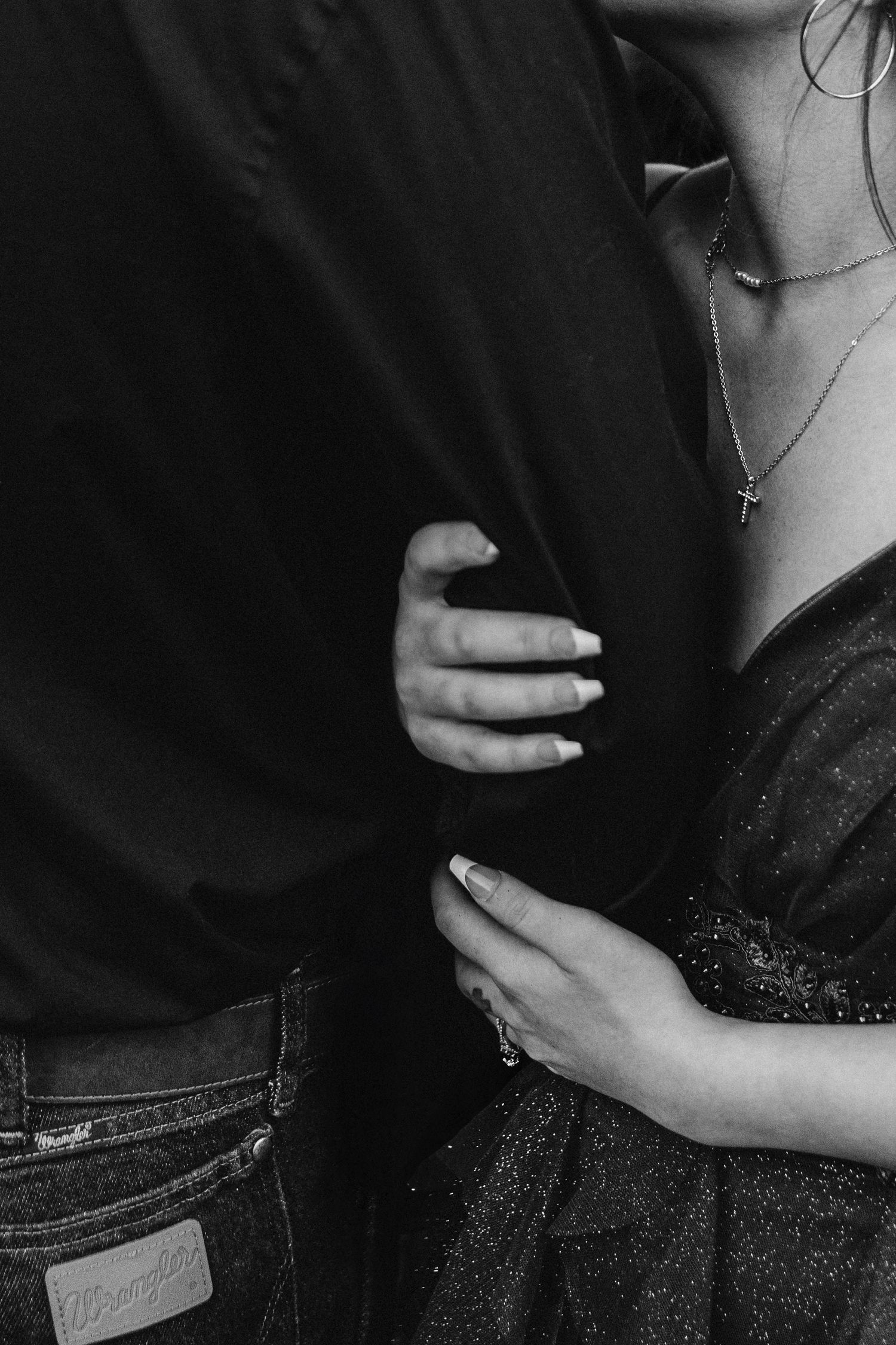 Black and white close-up of hands gently embracing with delicate jewelry visible.