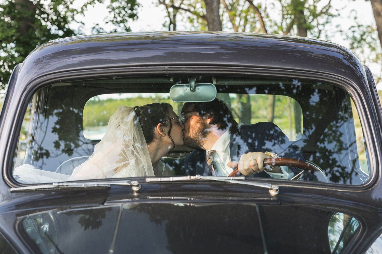 Newlywed couple sharing a romantic kiss inside a vintage black car, bride wearing a white veil.