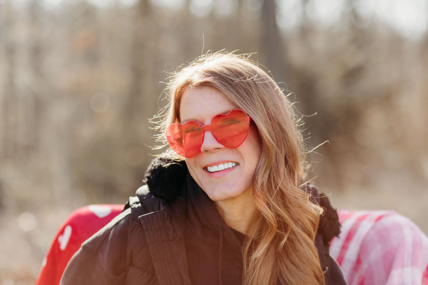 Woman in red sunglasses and pink sweater smiling outdoors in winter setting.