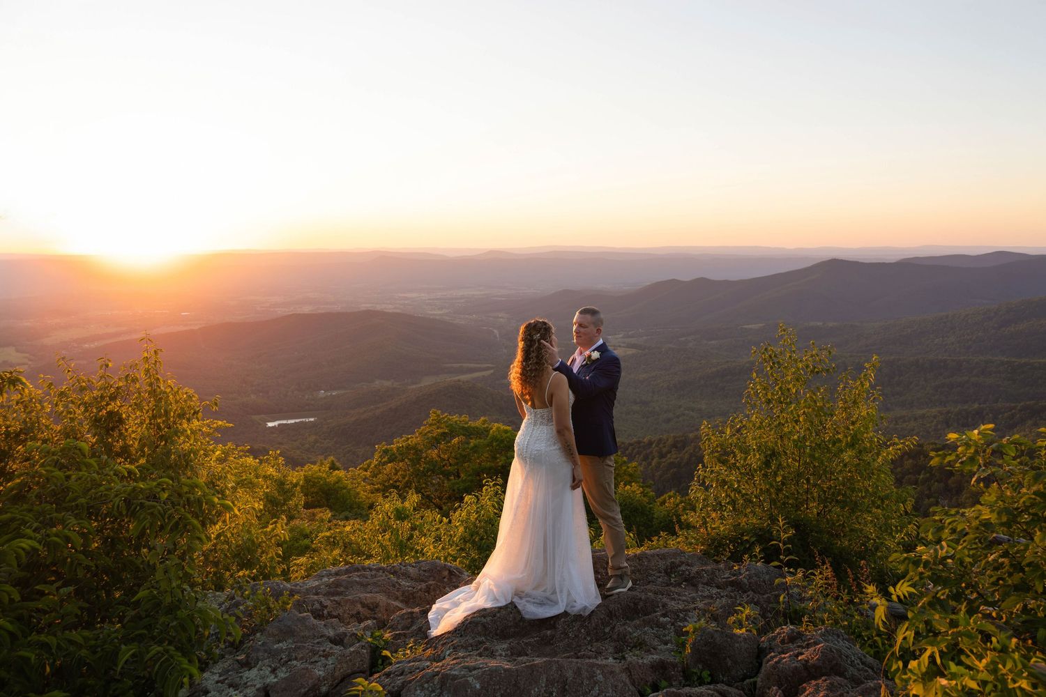 Bride and groom share a romantic sunset moment on a mountain overlook with sweeping valley views.