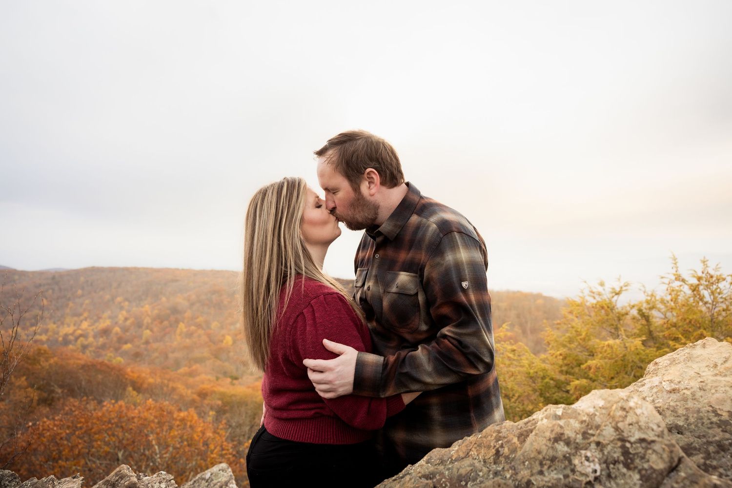 A romantic couple shares an intimate moment on a mountaintop overlook during golden hour in autumn.