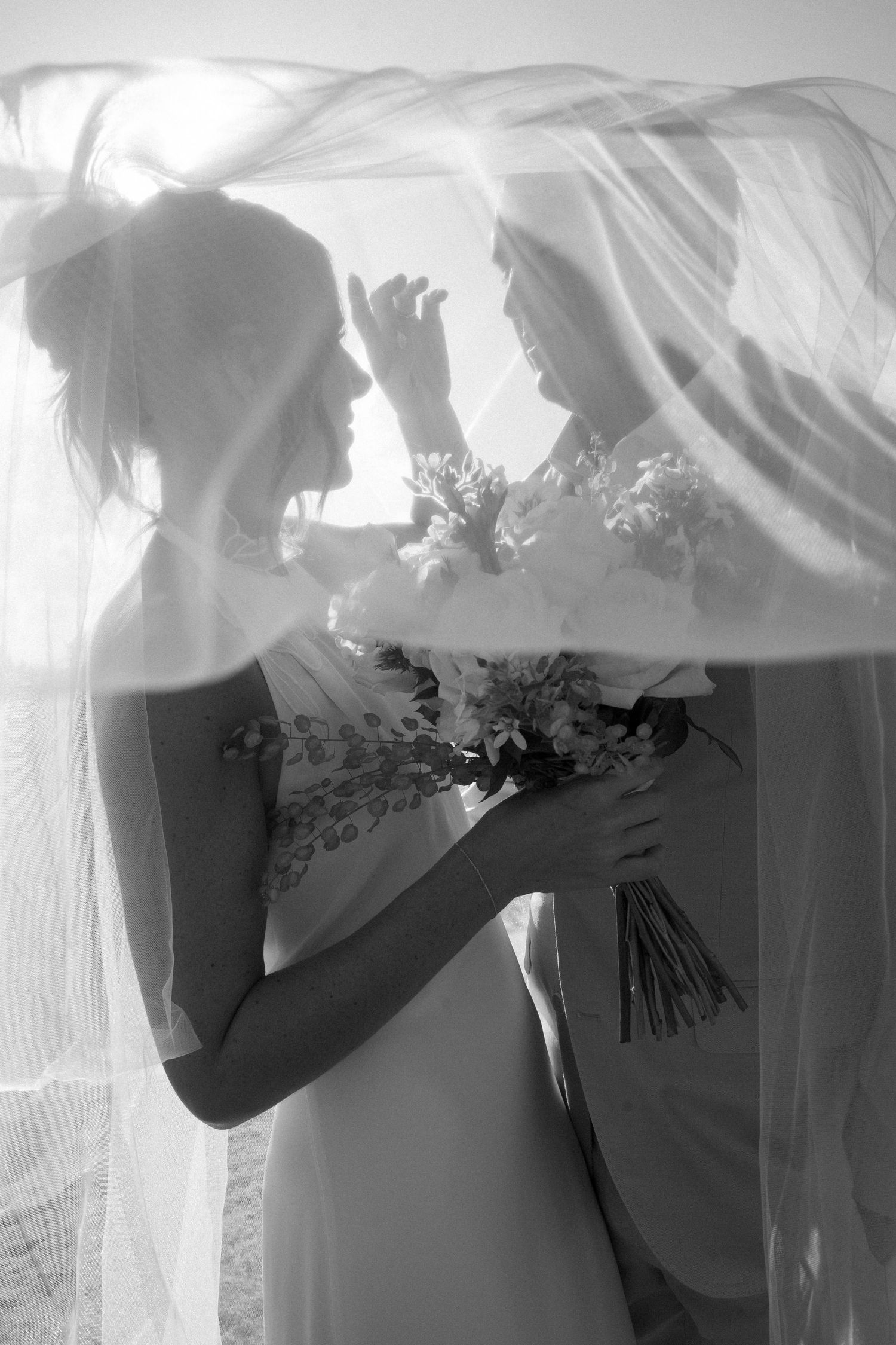 A series of black and white artistic photos showing a bride under flowing veil fabric in different ethereal poses.