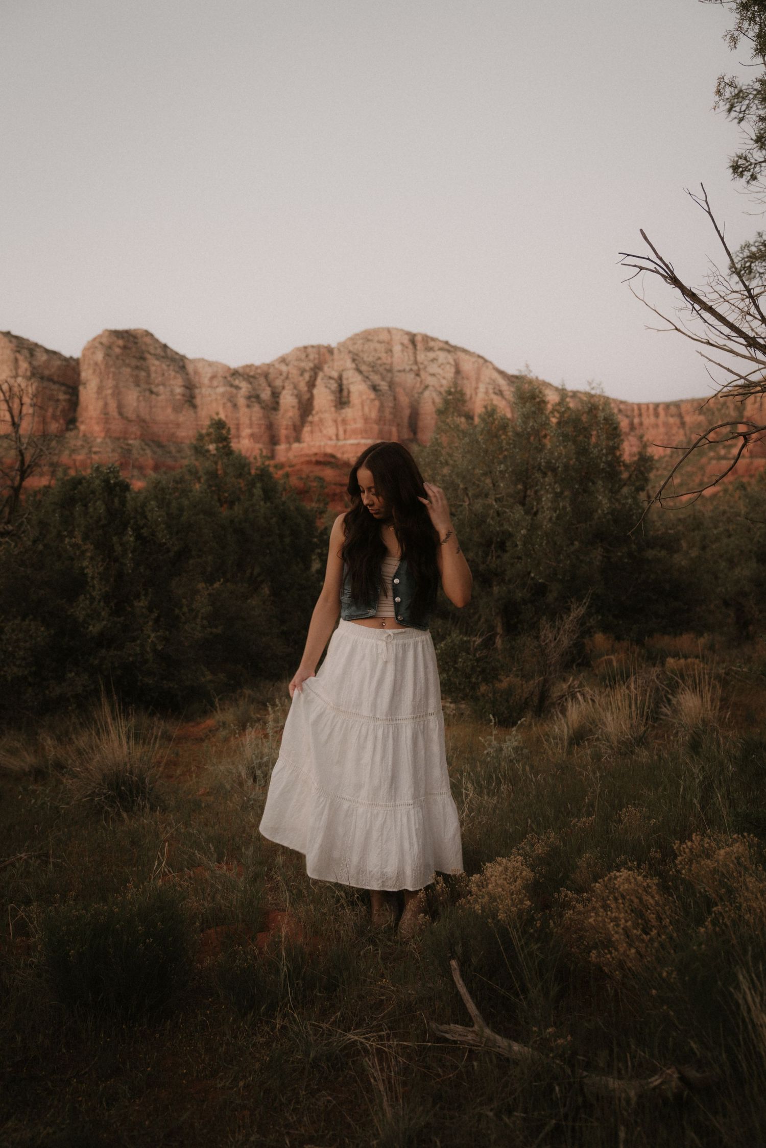 A dreamy portrait in a white dress against red rock mountains and desert brush at sunset.