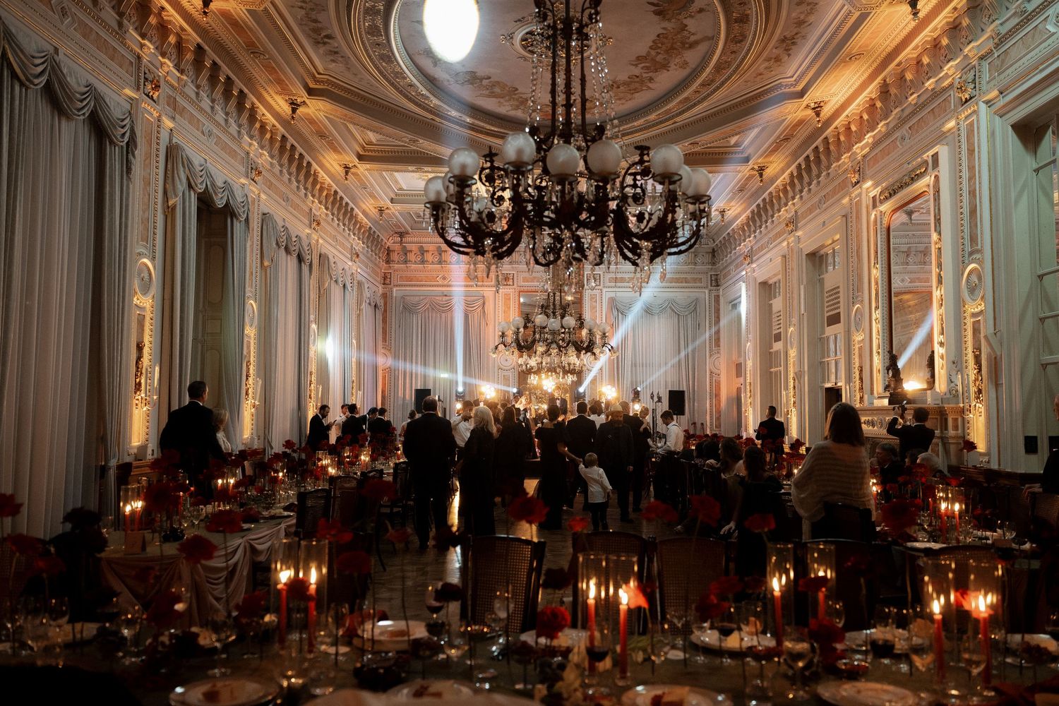 Elegant candlelit ballroom with ornate ceiling, chandelier, and guests gathered for a formal dinner event.