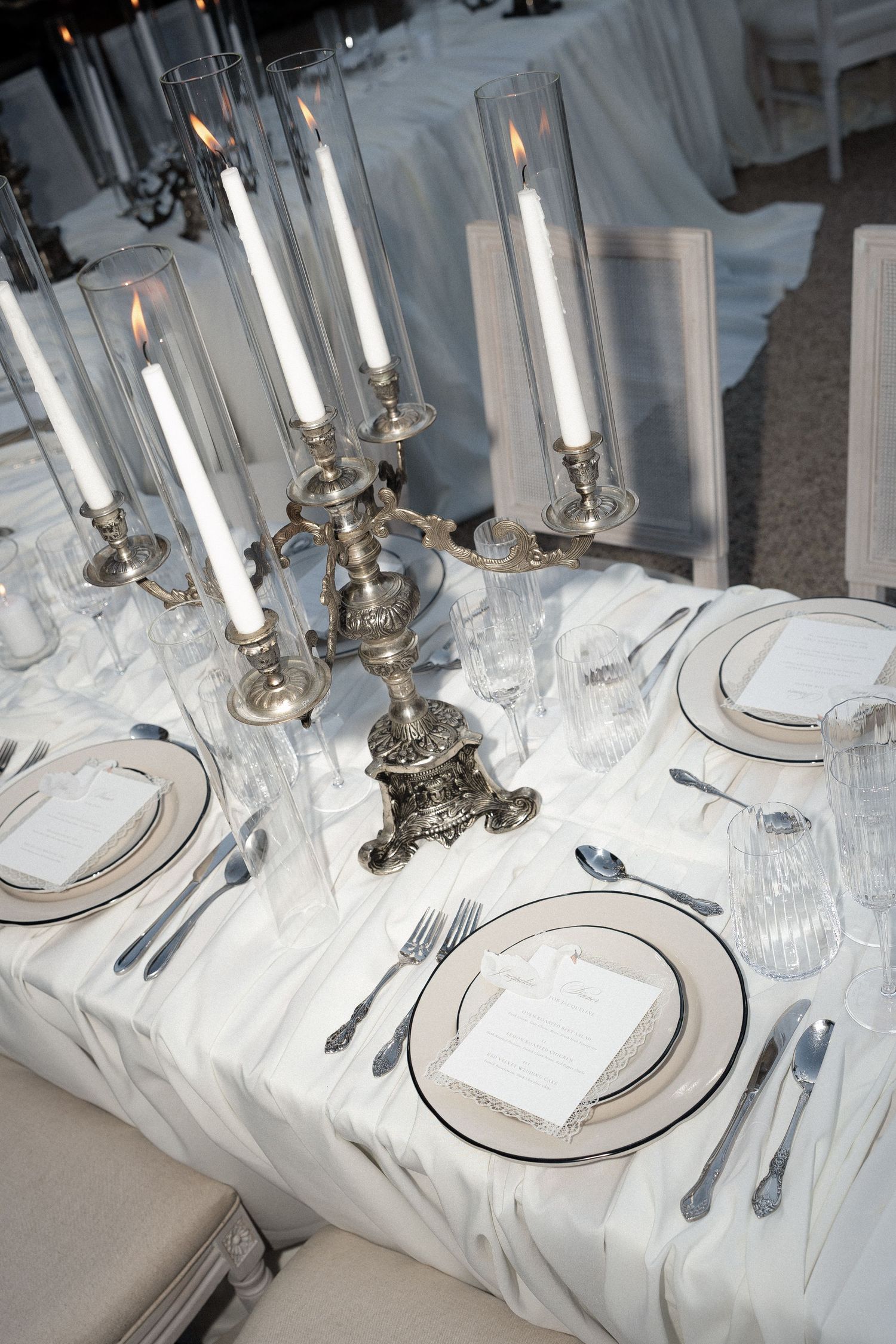Elegant white table setting with silver candelabras, white linens, and formal place settings arranged for a formal dinner.