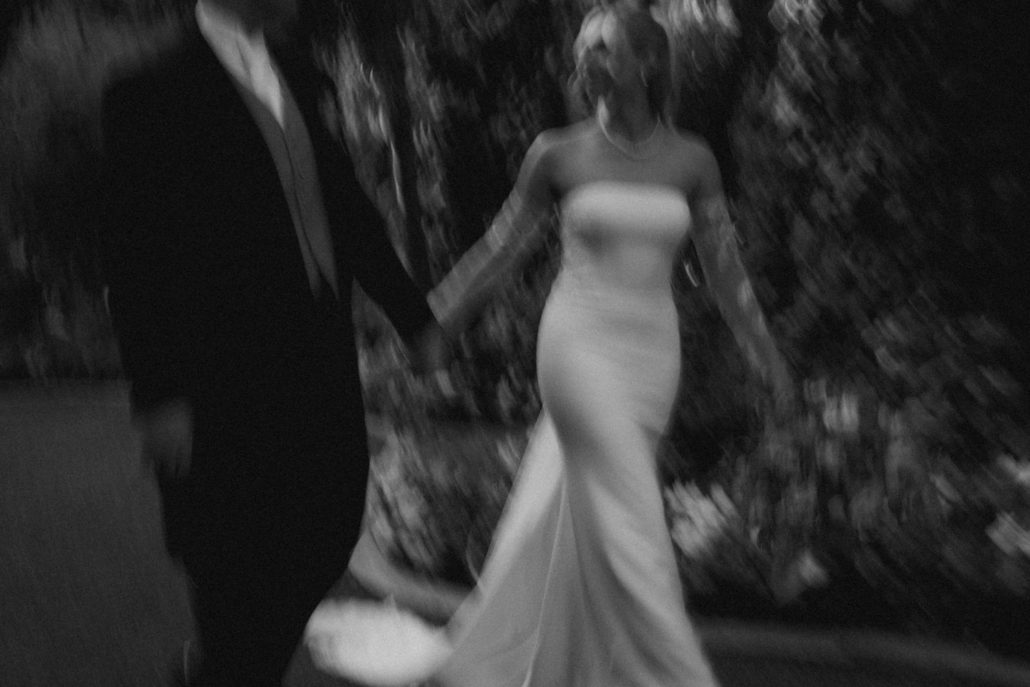 An artistic blurred black and white capture of a bride in a fitted wedding gown.