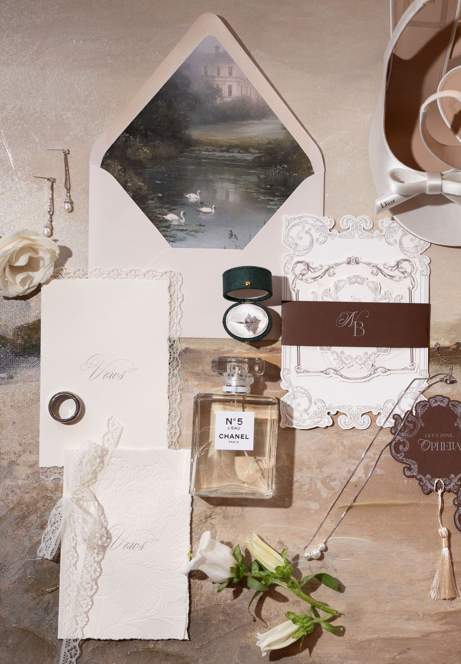 Vintage-style flat lay photography setup with perfume bottles, paper decorations, and greenery on a beige background.