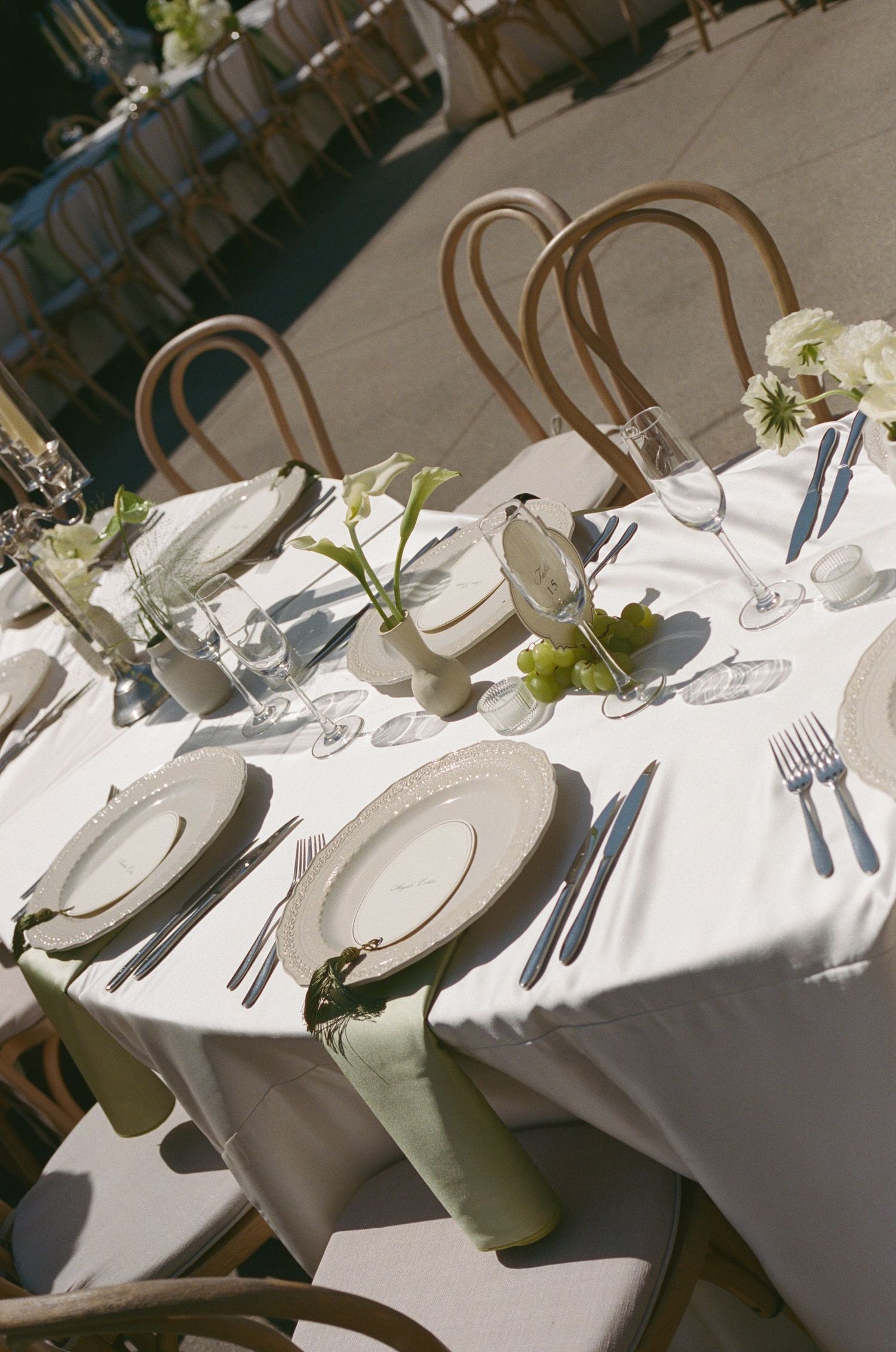 Elegant outdoor wedding reception table set with white linens, green napkins, floral centerpieces, and fine dining place settings.