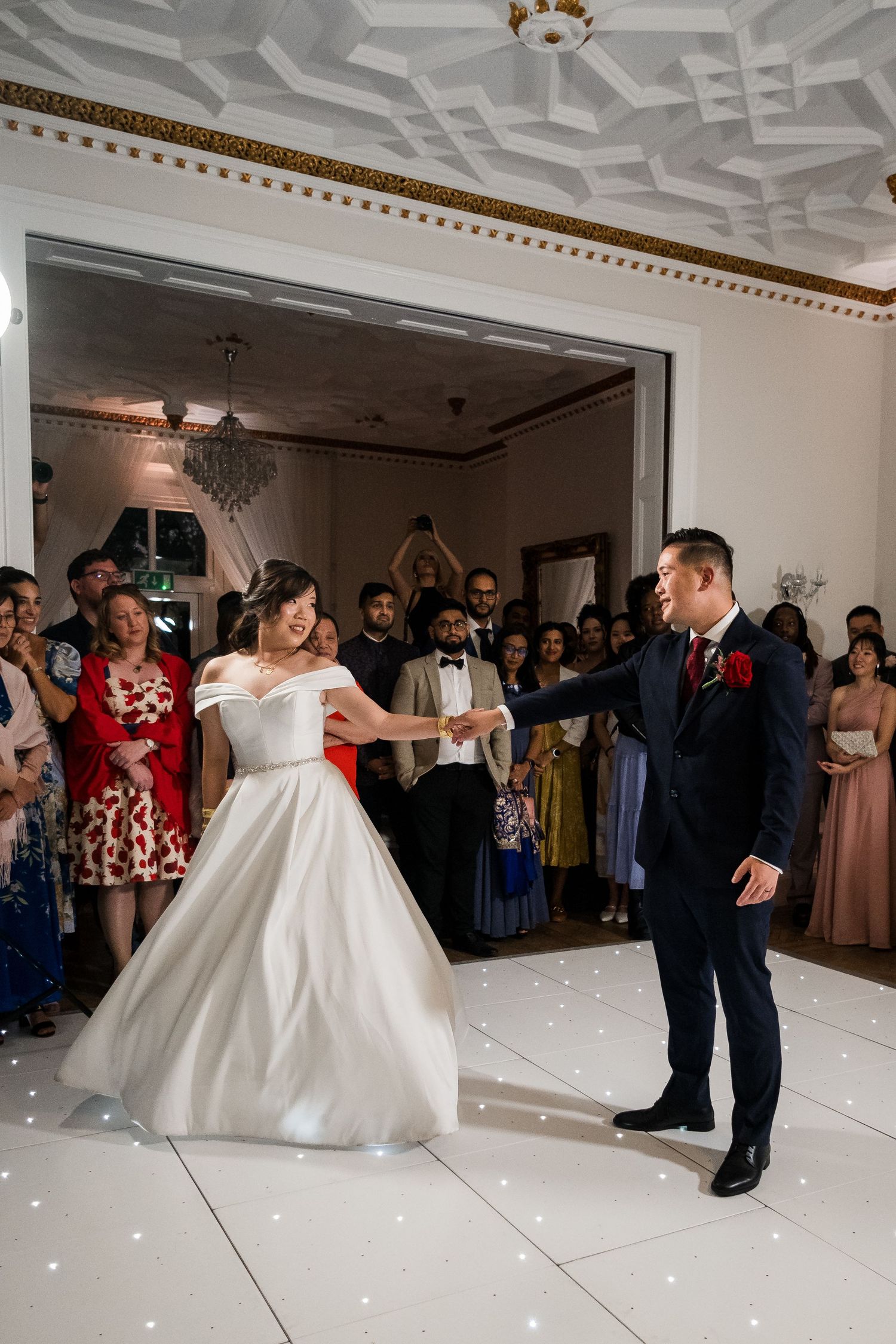 A couple performs an elegant dance spin during their first dance at a wedding reception with guests watching.