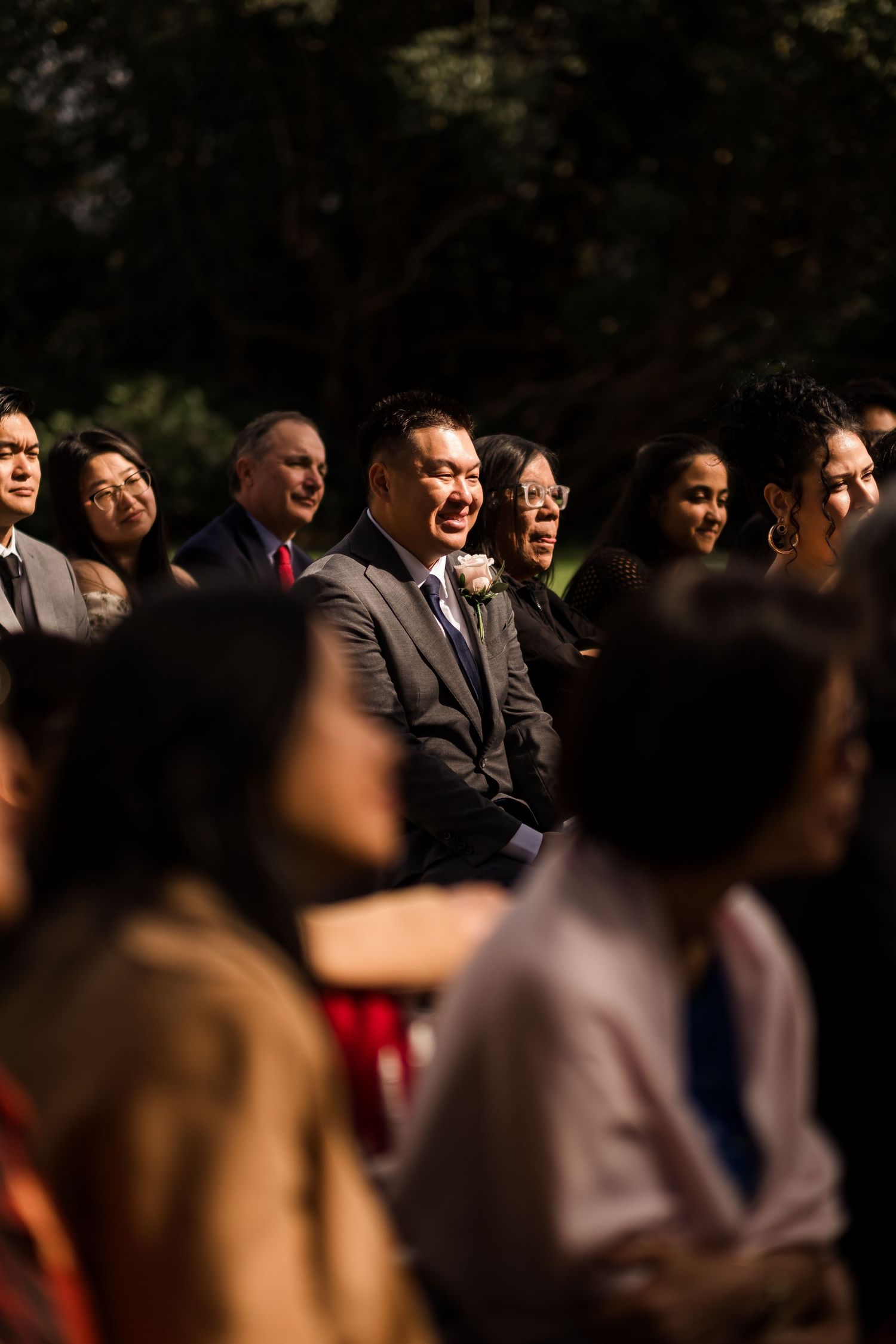A crowd of people gathered outdoors in sunlight casting dramatic shadows across their faces.