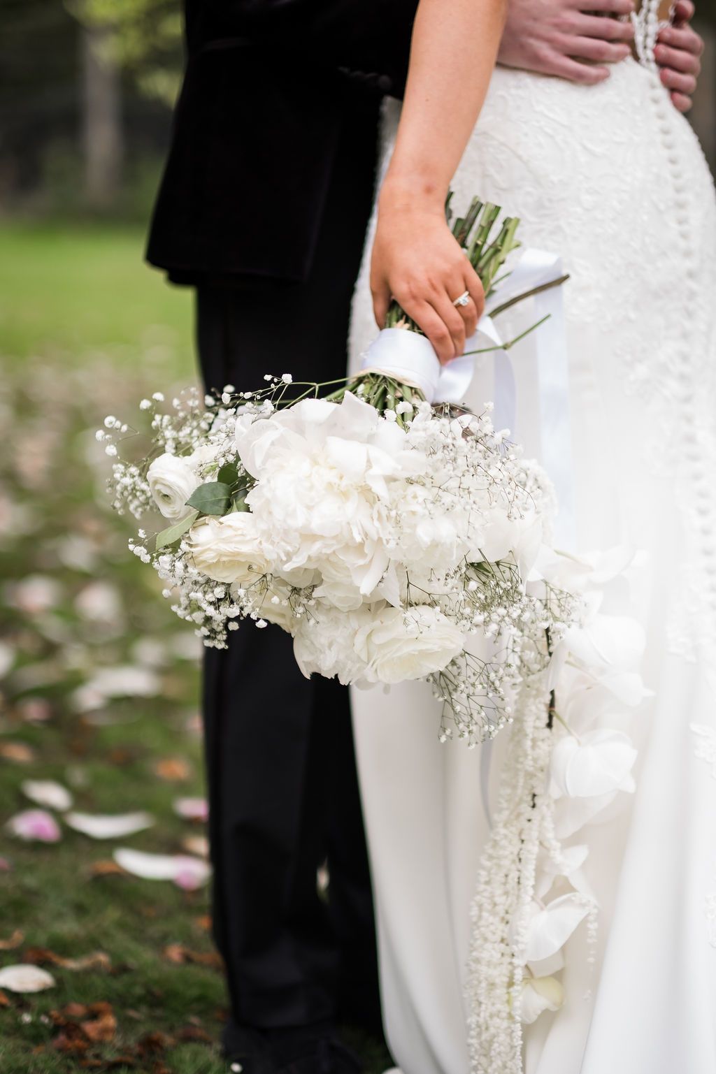 Close-up view of an elegant white wedding bouquet with baby's breath and calla lilies held against a white dress.