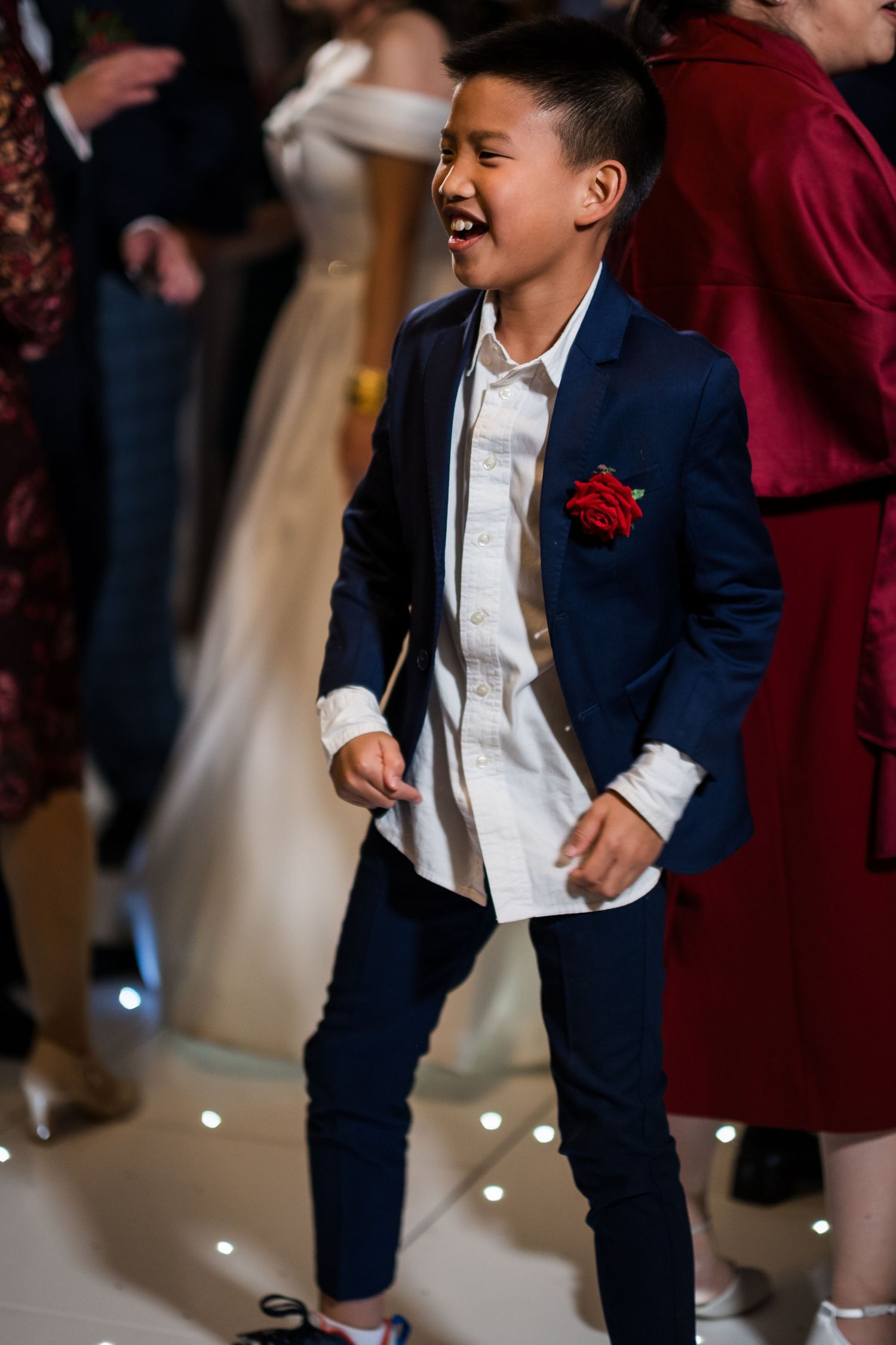 Young guest in navy blue blazer with red boutonniere dances joyfully at formal event.