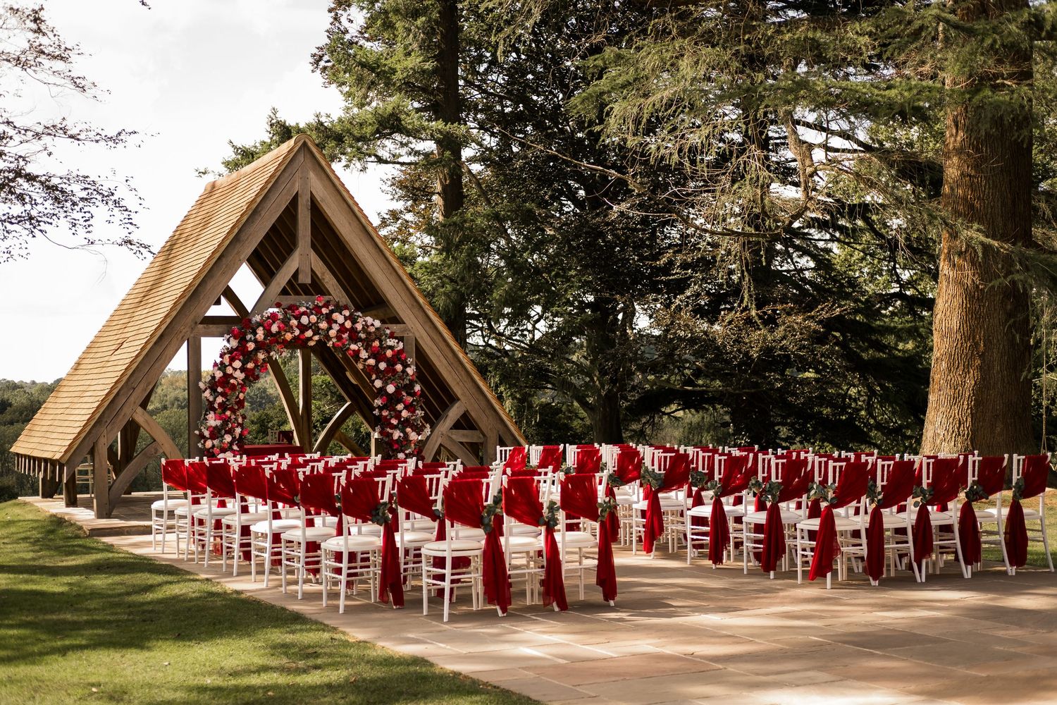 Outdoor garden ceremony at Highley Manor decorated with red flowers and draped chairs.