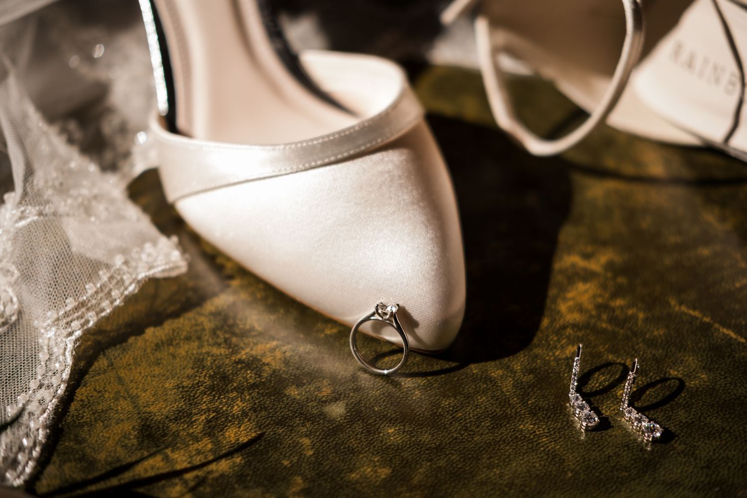 Wedding rings and elegant white bridal shoes displayed on a rustic surface with delicate lace details.