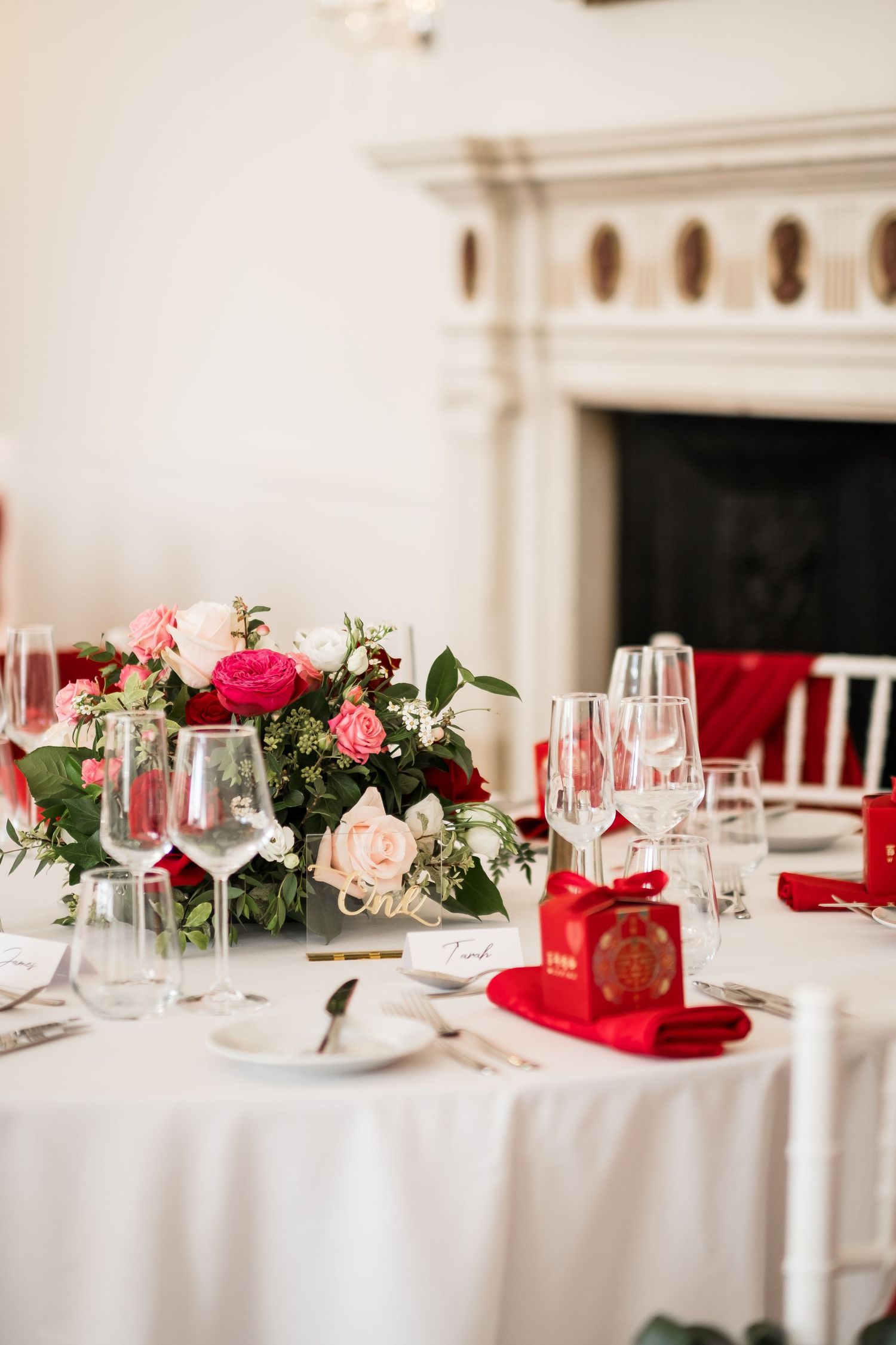 Elegant wedding table setting with pink and red floral centerpiece, white linens, wine glasses and red napkin accents.